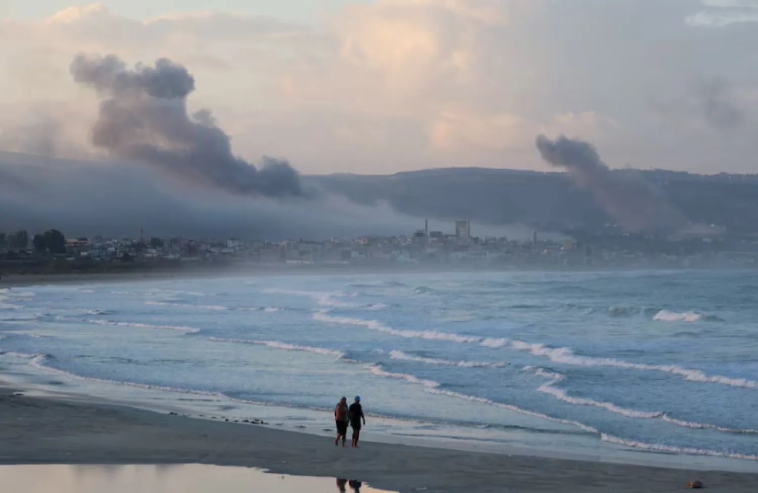 People walk at a beach as smoke billows over southern Lebanon following Israeli strikes, amid ongoing cross-border hostilities between Hezbollah and Israeli forces, as seen from Tyre, southern Lebanon September 23, 2024. REUTERS