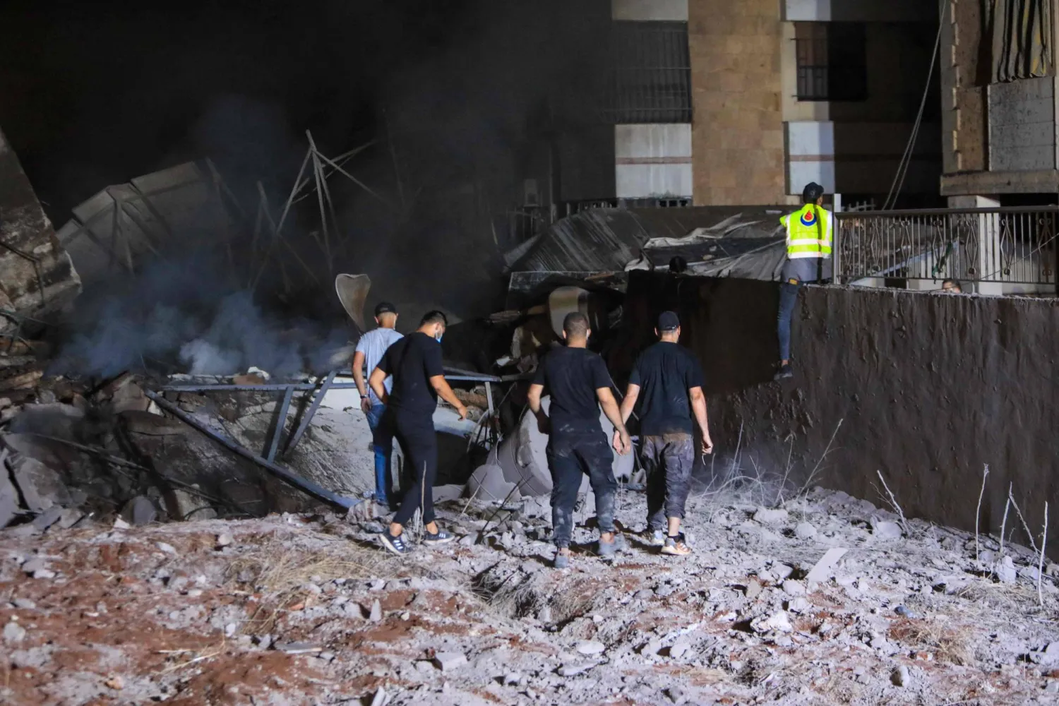 أشخاص ومُسعفون يقفون على أنقاض مبنى دمرته غارة إسرائيلية على الضاحية الجنوبية لبيروت (أ.ف.ب)