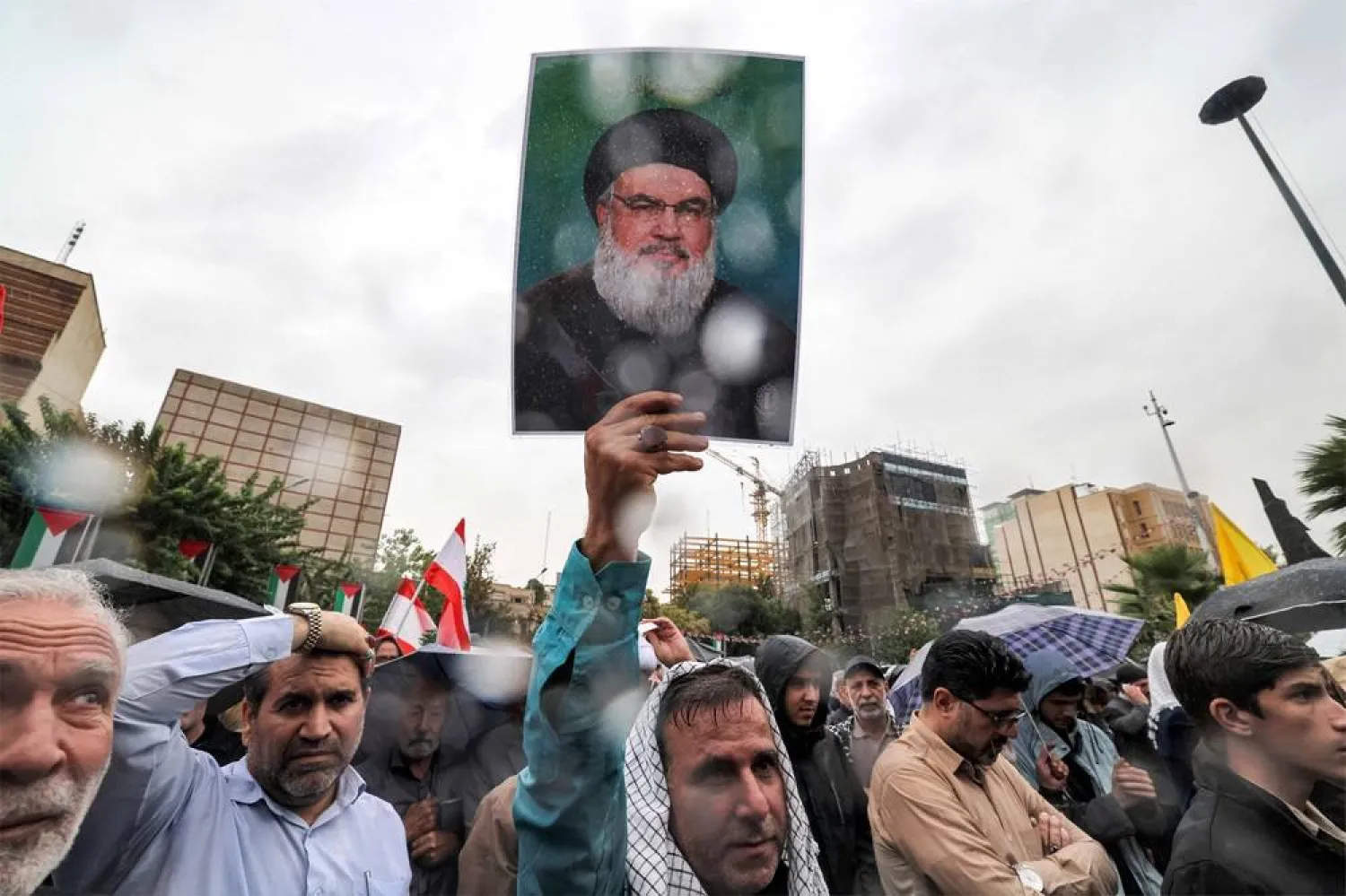 A demonstrator stands in the rain holding up a picture of late Lebanese Hezbollah leader Hassan Nasrallah who was killed by an Israeli air strike the previous day, during an anti-Israel protest in Tehran's Palestine Square on September 28, 2024. (AFP) 