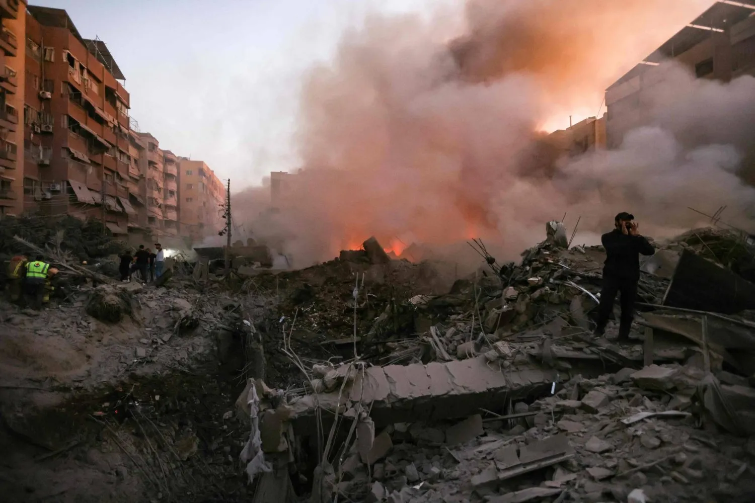İsrail'in Hizbullah karargahına düzenlediği hava saldırısında yıkılan bir binanın yanan enkazının yakınında toplanan insanlar ve kurtarma ekipleri (AFP)