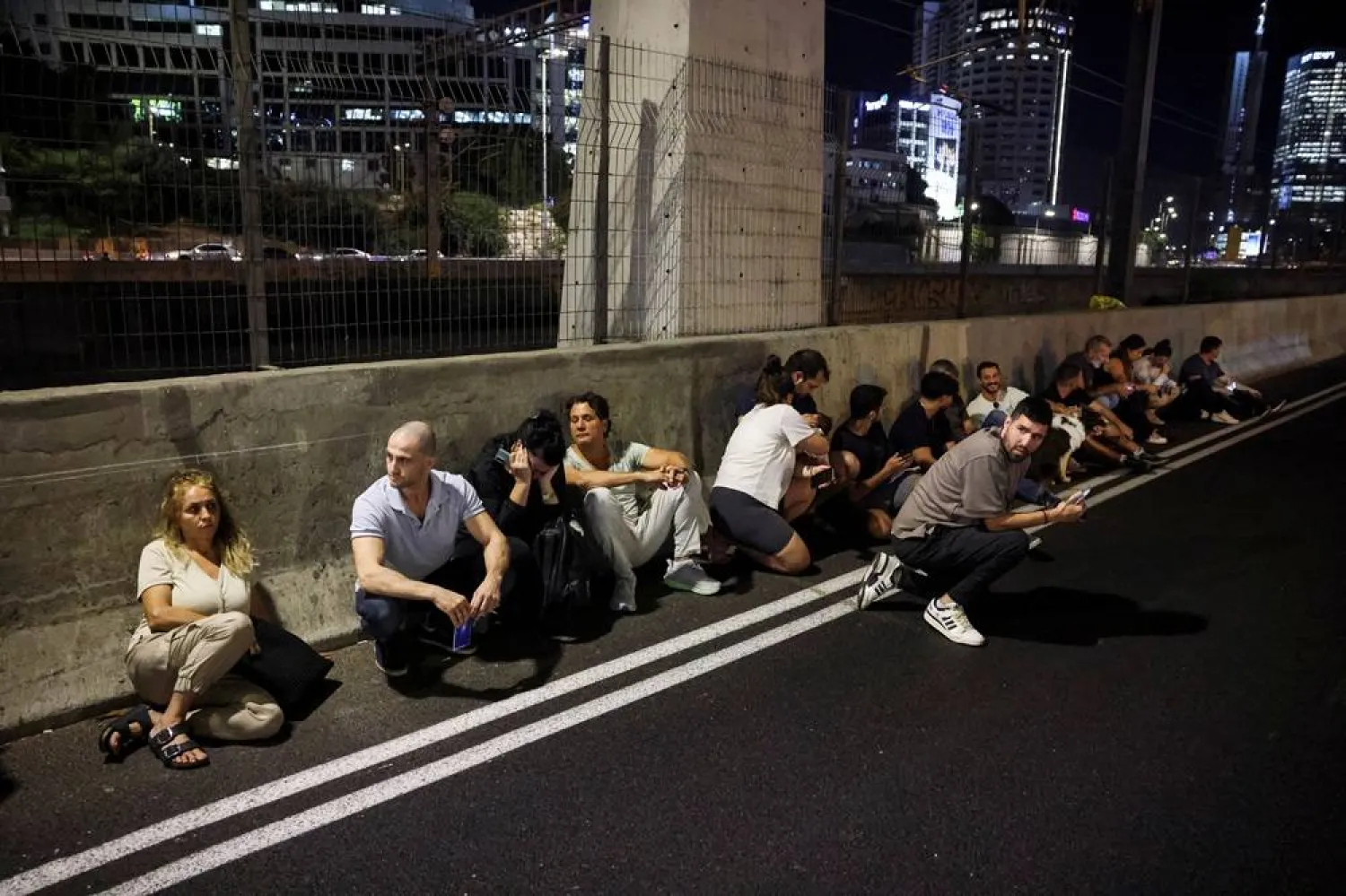 People take cover by the side of a road as a siren sound, after Iran fired a salvo of ballistic missiles at Israel, in Tel Aviv, Israel, October 1, 2024. (Reuters)