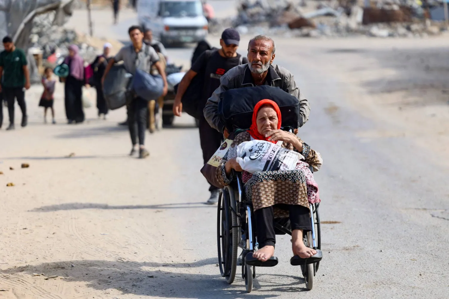 رجل يدفع سيدة على كرسي متحرك خلال الفرار من شمال مدينة غزة وسط الحرب الإسرائيلية (أ.ف.ب)