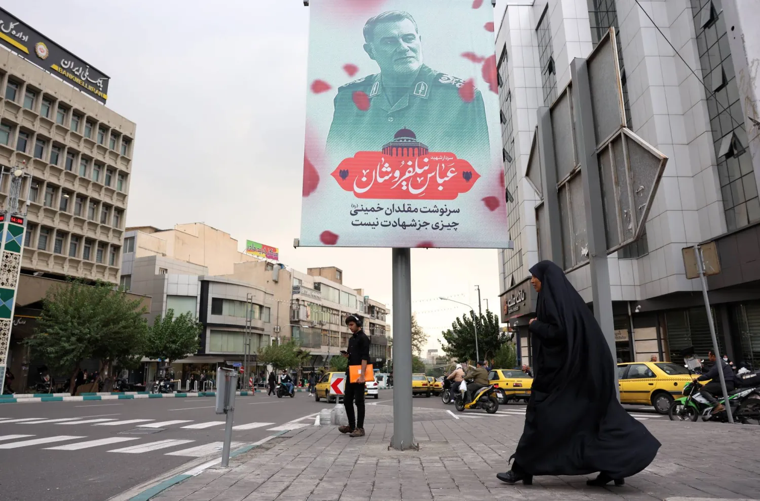 إيرانية بجوار ملصق يحمل صورة عباس نيلفروشان في طهران (إ.ب.أ)