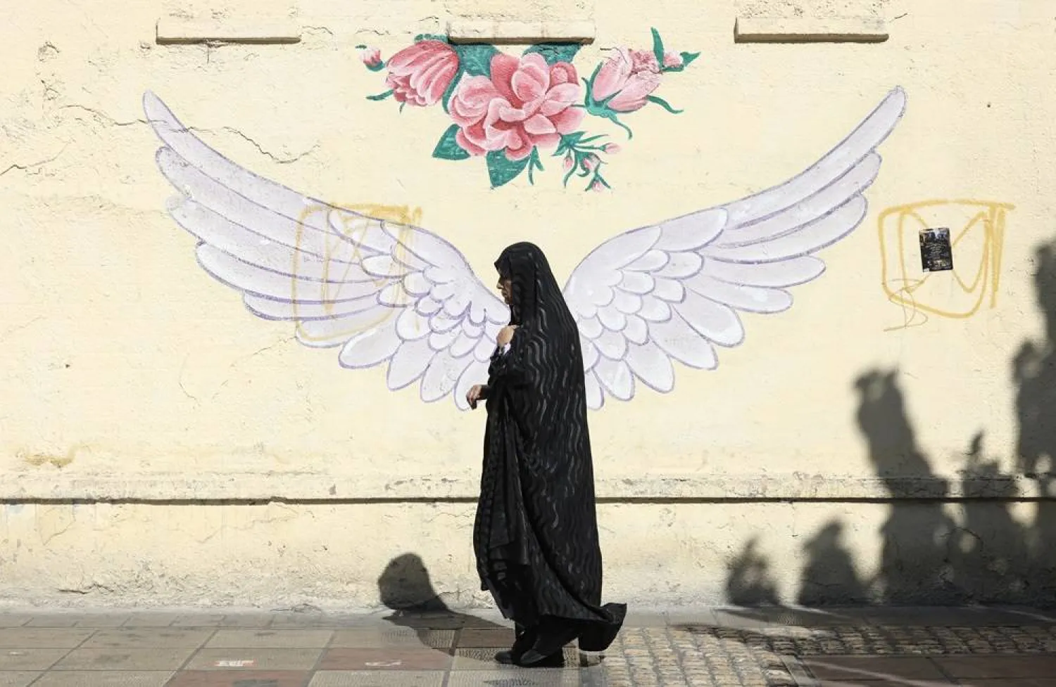 A veiled Iranian woman walks past a mural in a street in Tehran, Iran, 07 October 2024. (EPA)