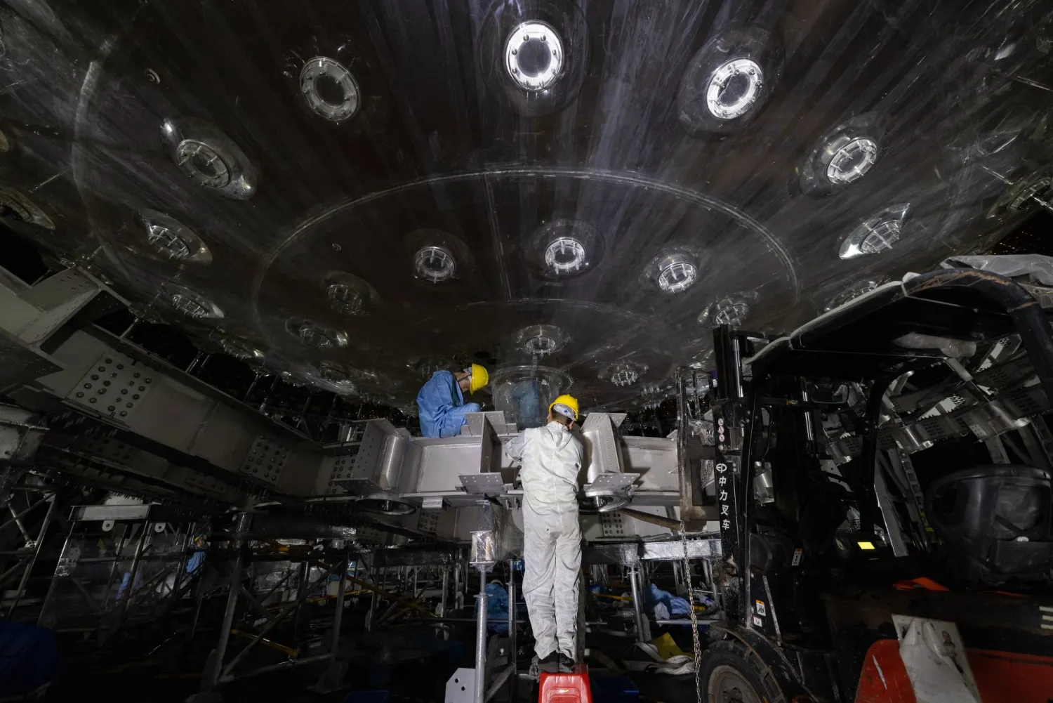 أعضاء فريق يقومون بتركيب الجزء الخارجي لإطار من الفولاذ المقاوم للصدأ لجهاز الكشف المركزي لمرصد جيانغمن للنيوترينوات تحت الأرض (جونو) بمقاطعة قوانغدونغ جنوب الصين (إ.ب.أ)