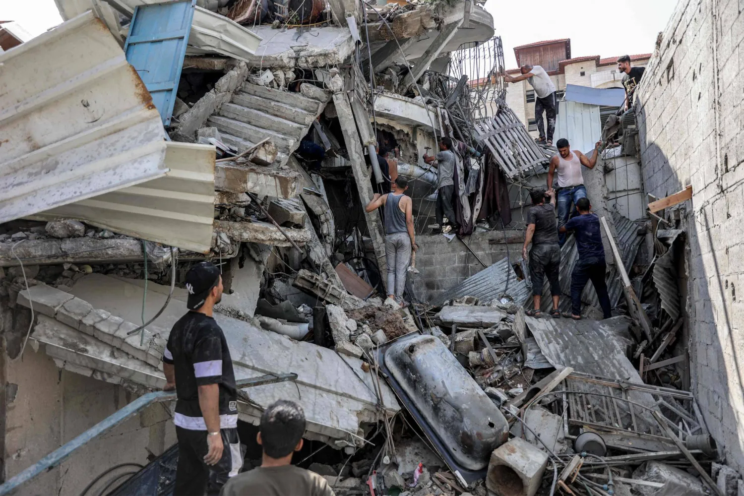 People gather outside a collapsed building as they attempt to extricate a man from underneath the rubble following Israeli bombardment in the Saftawi district in Jabalia in the northern Gaza Strip on October 15, 2024 amid the ongoing war in the Palestinian territory between Israel and Hamas. (Photo by Omar AL-QATTAA / AFP)
