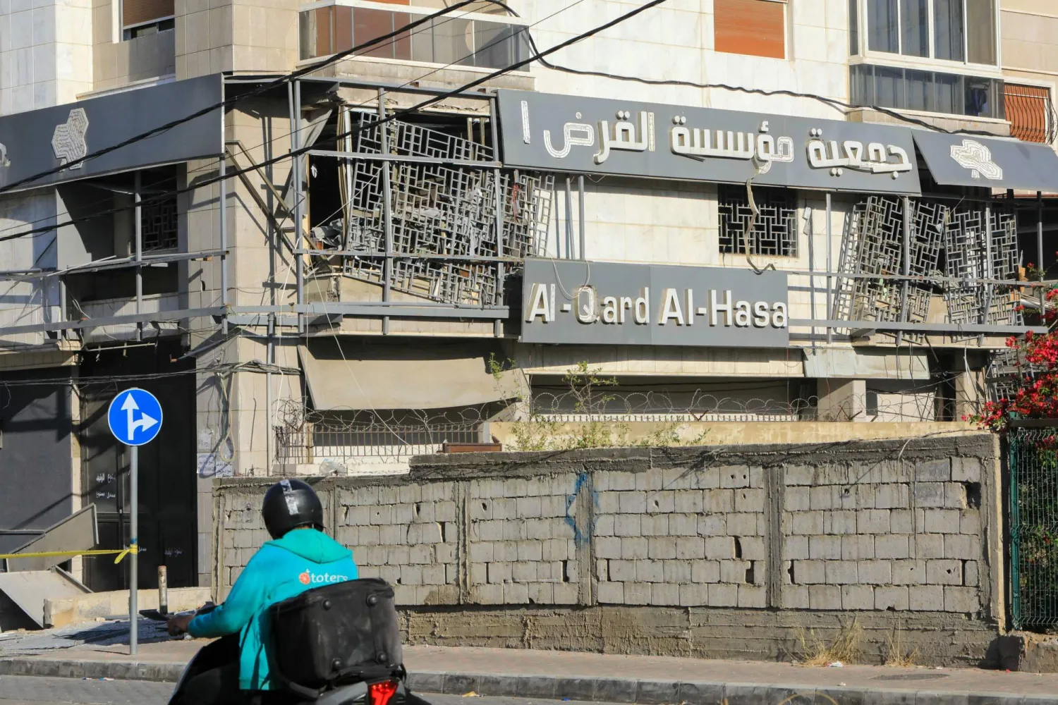 رجل يقود دراجته النارية أمام موقع غارة جوية إسرائيلية ليلية استهدفت فرعاً لمجموعة «القرض الحسن» للتمويل في الضاحية الجنوبية لبيروت الاثنين (أ.ف.ب)