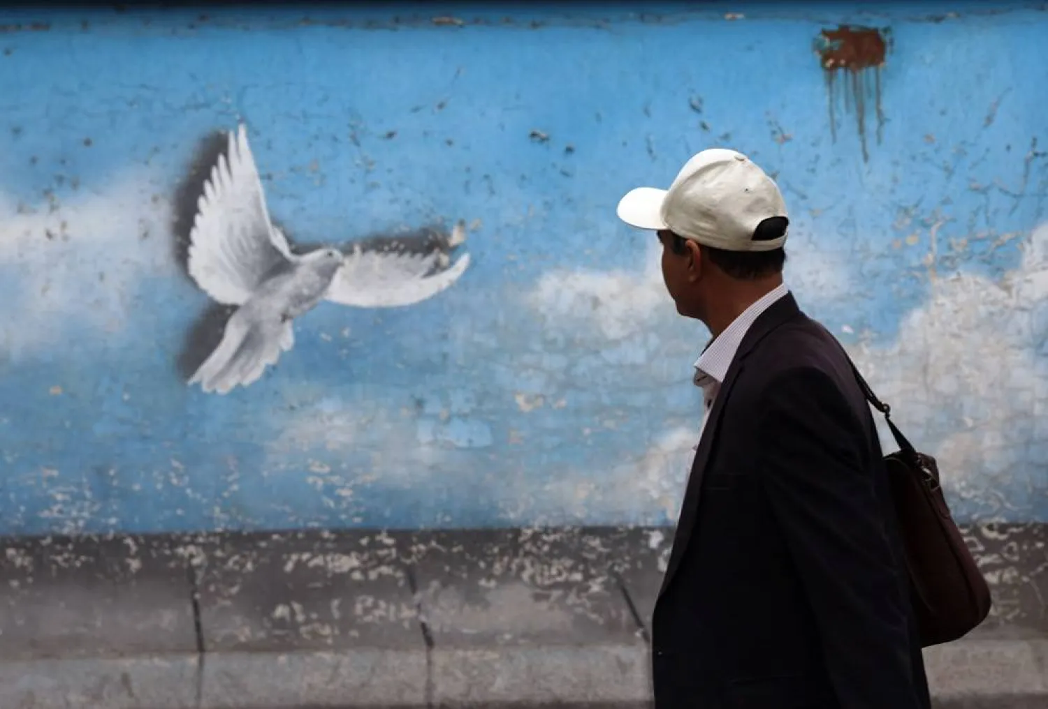 An Iranian man walks past a wall painting of a peace bird in Tehran, Iran, 21 October 2024. (EPA)