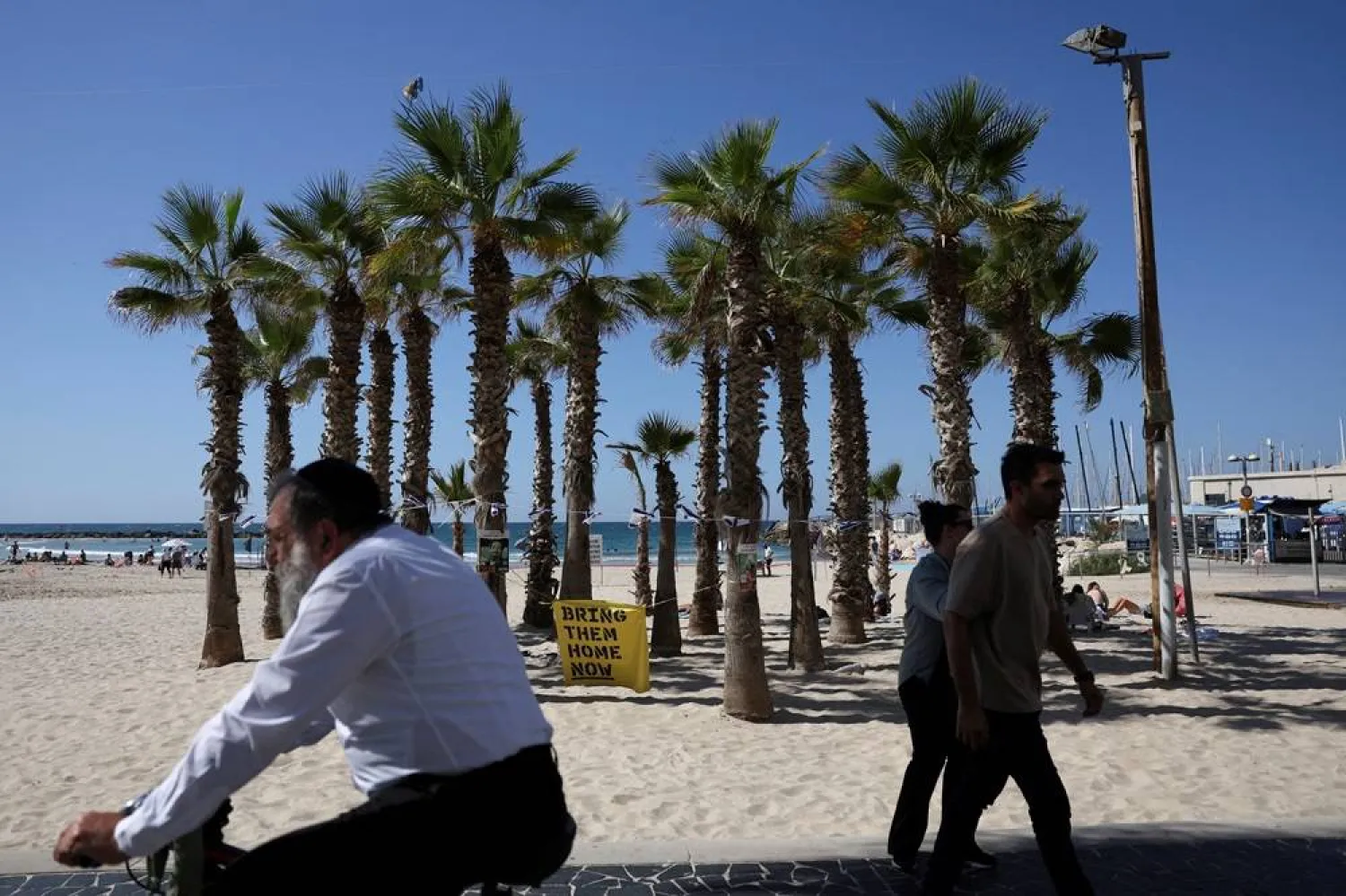 People pass by a poster reading "Bring them home now" on a beach, in Tel Aviv, Israel, October 20, 2024. (Reuters)