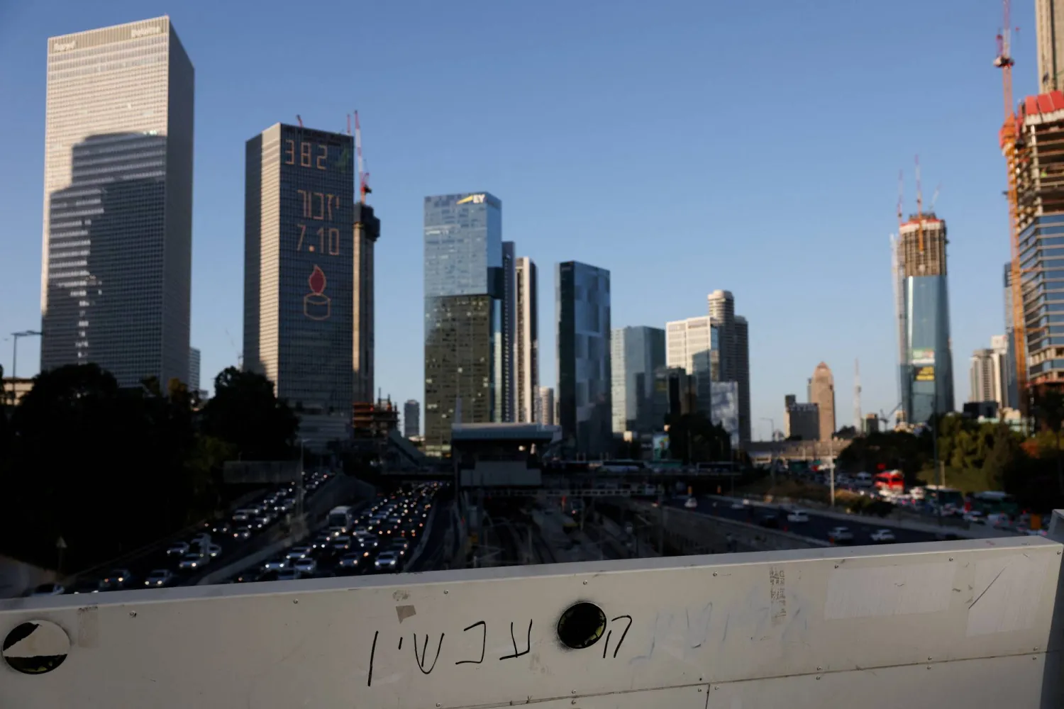 A view shows graffiti, partially painted over, on a bridge overlooking the city's main highway, near a building with a light display commemorating the deadly October 7, 2023, attack on Israel by Hamas, in Tel Aviv, Israel, October 22, 2024. REUTERS/Violeta Santos Moura