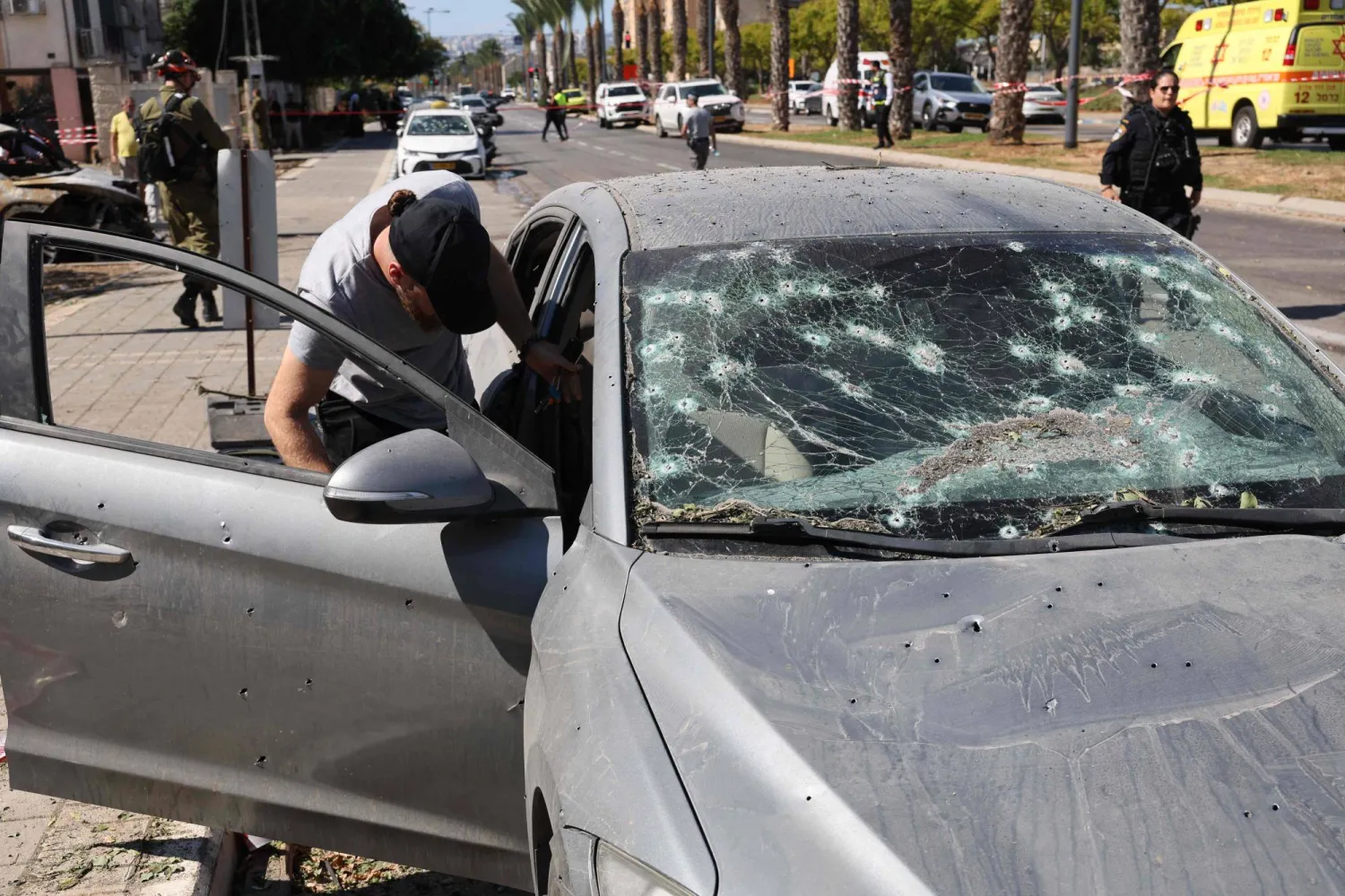 رجل يتفقد سيارته التي أصيبت بشظايا جراء إطلاق صاروخ من لبنان إلى مدينة حيفا غي إسرائيل (أ.ف.ب)
