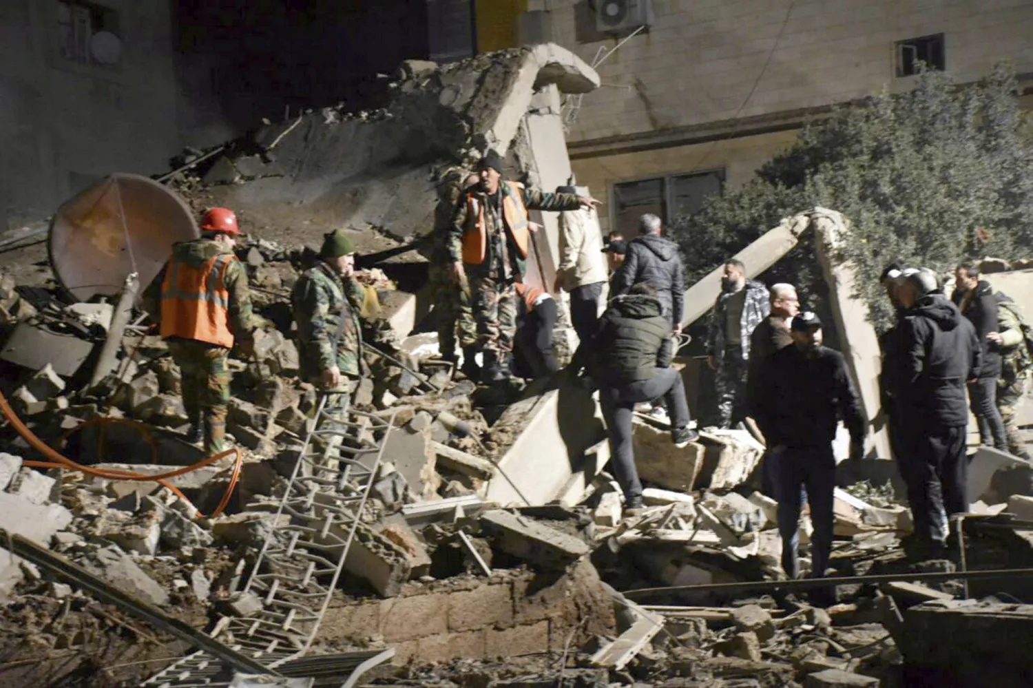 In this photo released by the Syrian official news agency SANA, Syrian security forces gather near the rubble of a building that was destroyed by Israeli airstrikes, in Homs, Syria, late Tuesday, Feb. 6, 2024. (SANA via AP)