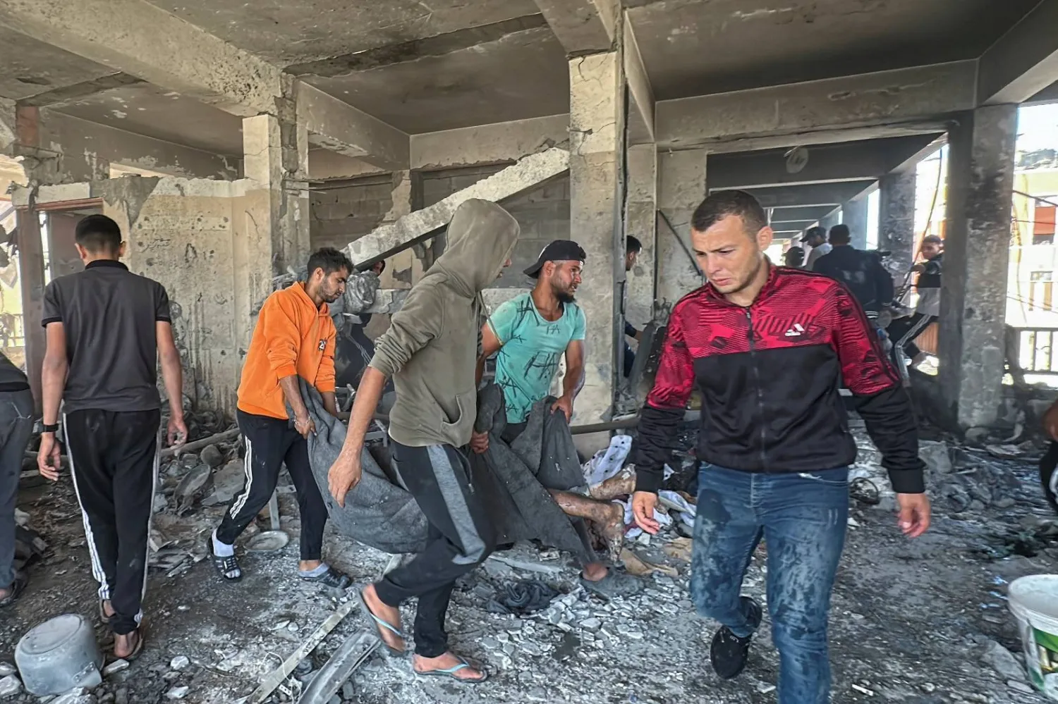 أشخاص يحملون جثة فلسطيني قُتل في غارة إسرائيلية على مدرسة تؤوي النازحين وسط قطاع غزة (رويترز)