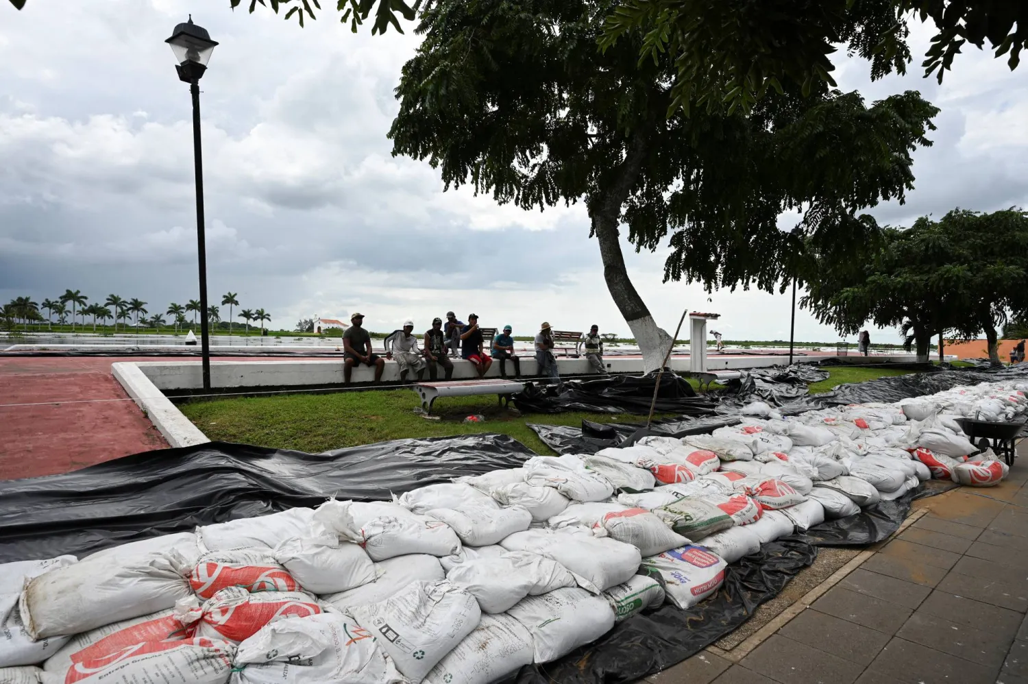 People sit near a barrier with sandbags as a precaution to prevent probable flooding caused by the overflowing of the Papaloapan river, as heavy rains are expected, in Tlacotalpan, Mexico, October 25, 2024. REUTERS/Yahir Ceballos