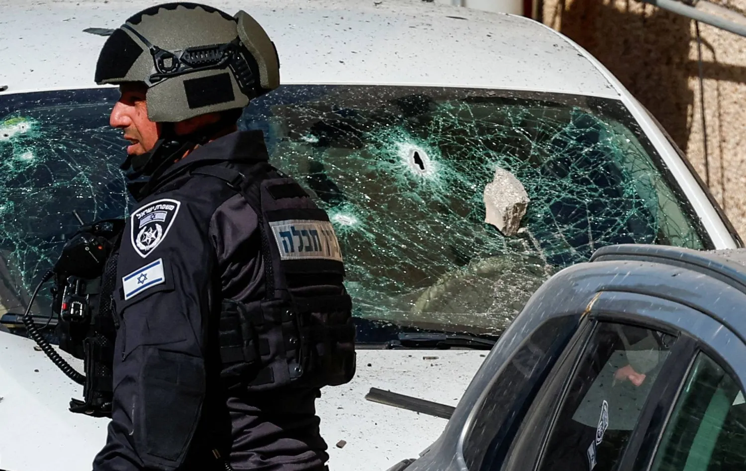 أحد أفراد قوات الأمن الإسرائيلية يقف بجوار سيارة متضررة في موقع هجوم بطائرة مسيرة شمال إسرائيل (رويترز)