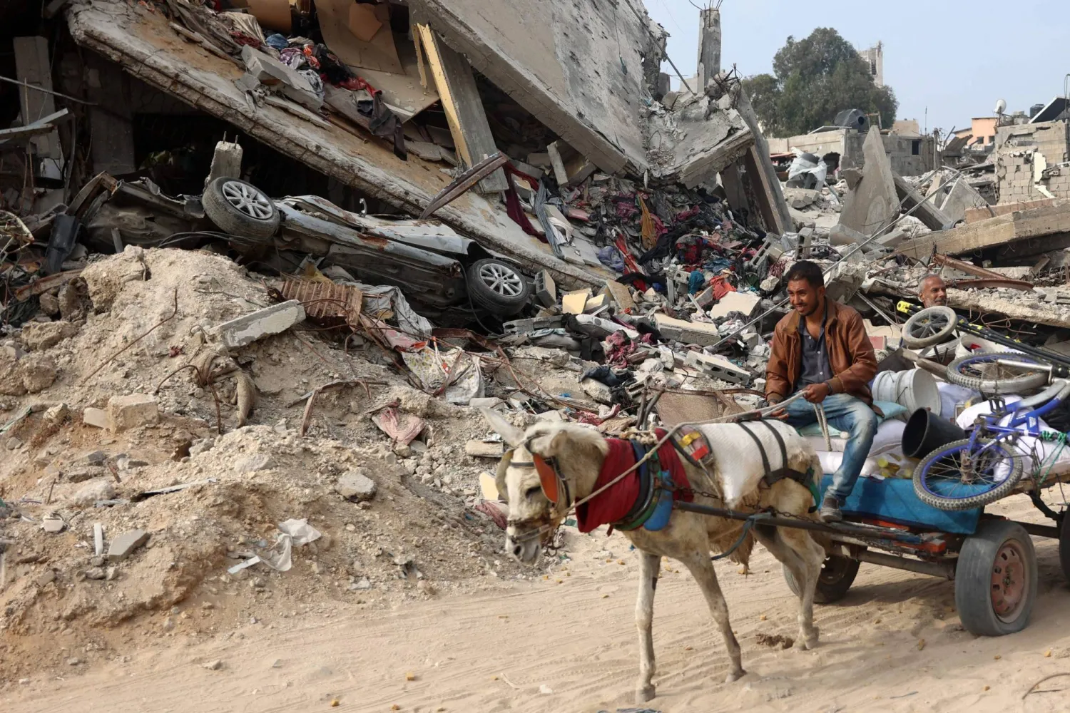 A Palestinian man rides a horse-pulled cart, next to a destroyed building where personal belongings of people and a car are sandwiched between the layers of its rubble, in Gaza City on November 2, 2024, amid the ongoing war between Israel and Hamas. (Photo by Omar AL-QATTAA / AFP)