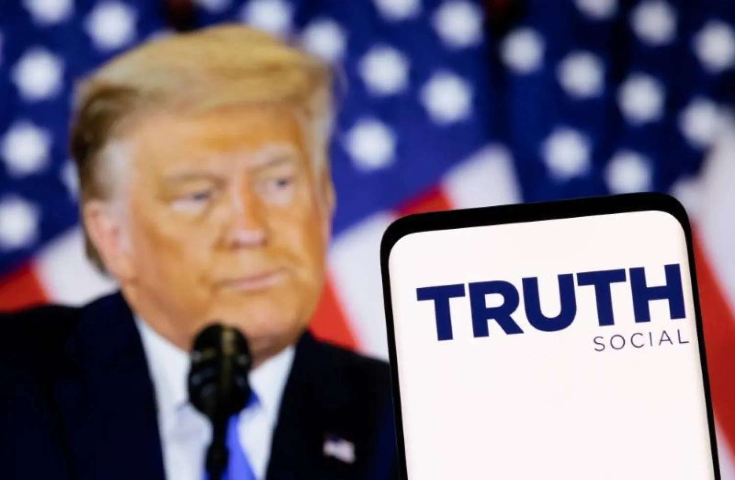 شعار شبكة «Truth» الاجتماعية يظهر على هاتف ذكي أمام صورة للرئيس الأميركي السابق دونالد ترمب (رويترز)