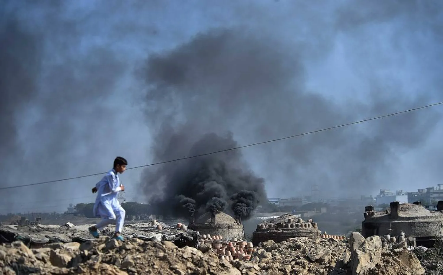 A boy runs as in the background smoke emits from a pottery factory in Karachi, Pakistan, 10 November 2024. (EPA)