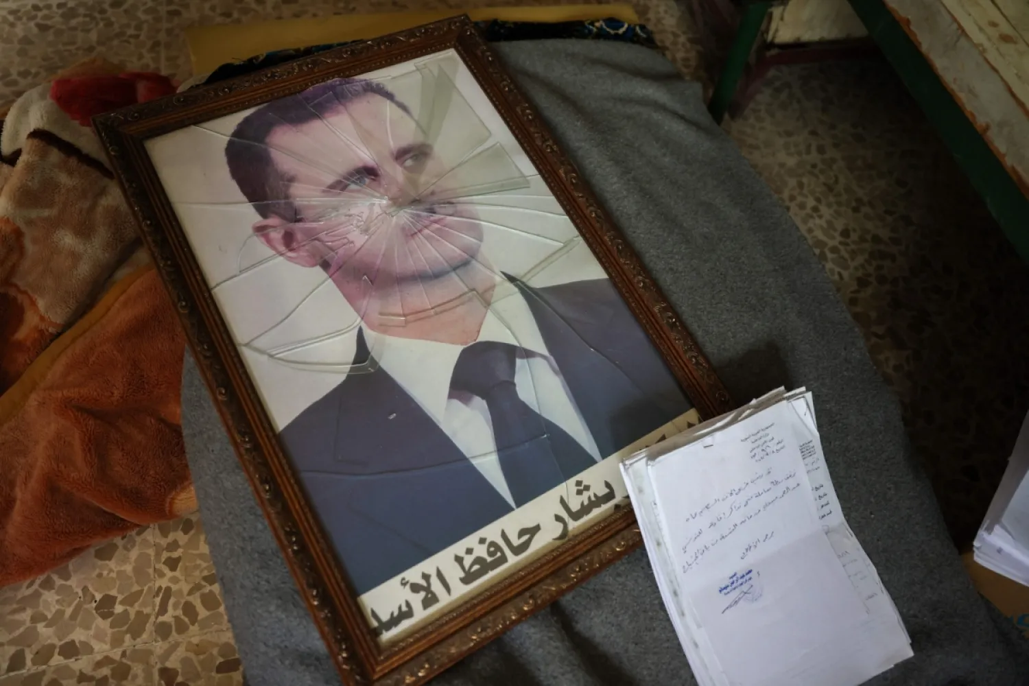Silahlı grupların bölgeyi kontrol altına almasının ardından Hama’nın dış mahallelerinde bulunan Siyasi Güvenlik Şubesi'ne ait bir tesiste Beşşar Esed'in çerçevesi kırılmış bir fotoğrafı, 7 Aralık 2024 (AFP)