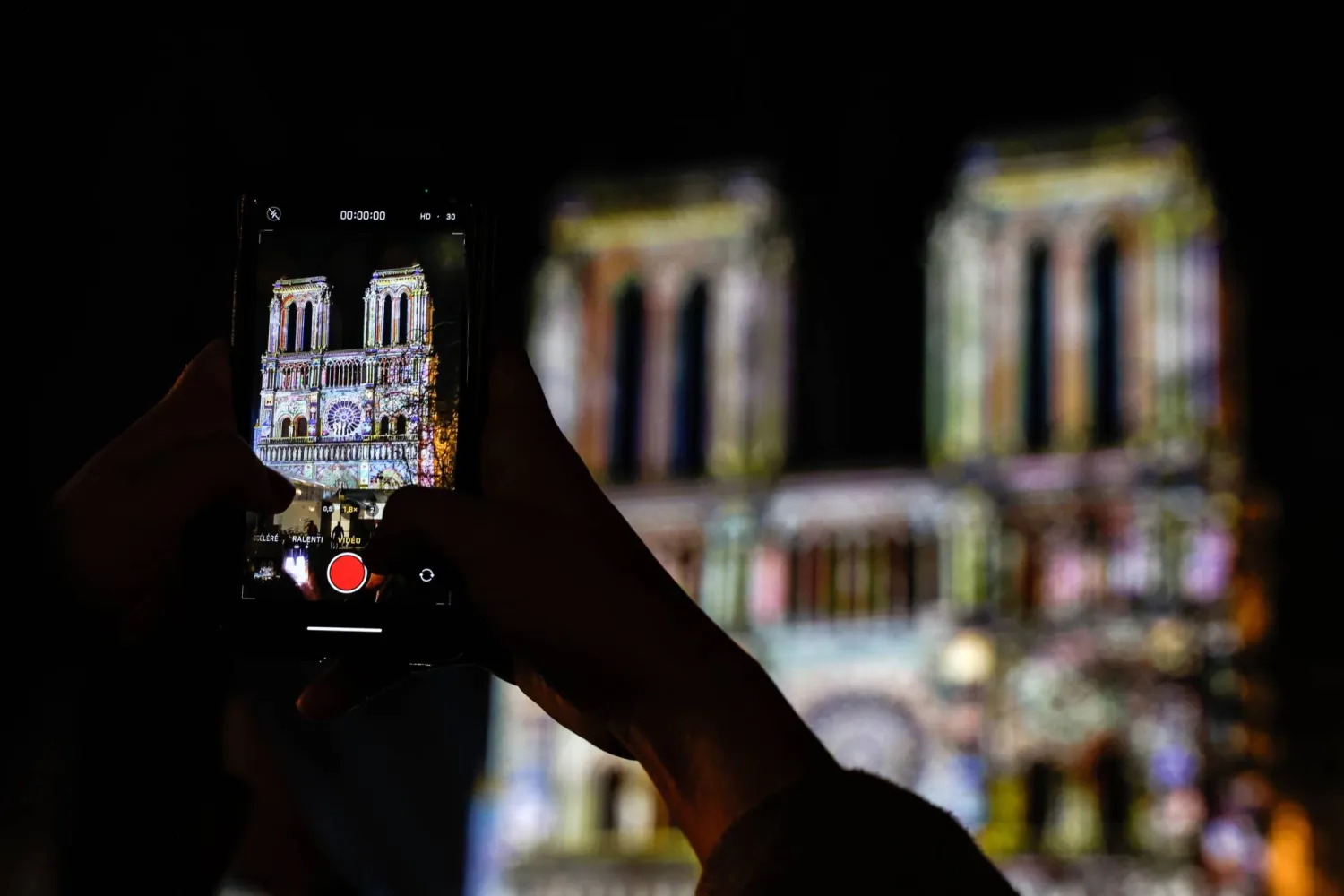 امرأة تلتقط مقطع فيديو لكاتدرائية نوتردام دو باري أثناء الاستعدادات النهائية لإعادة افتتاحها (إ.ب.أ)