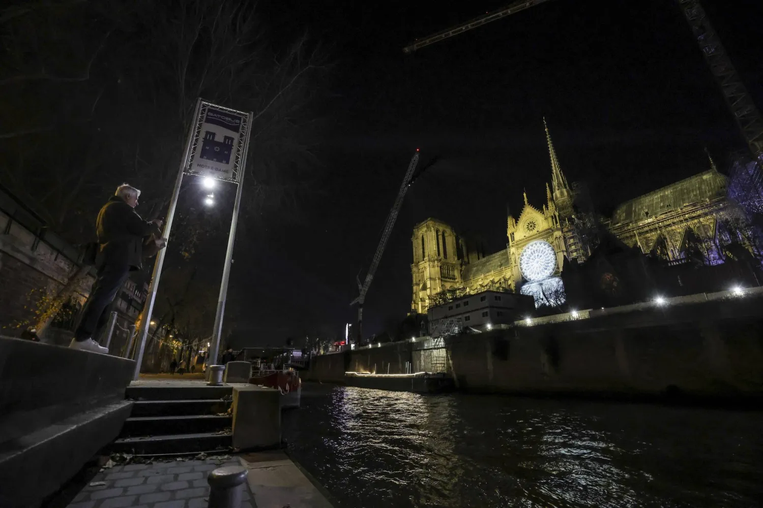 رجل يلتقط صورة لكاتدرائية نوتردام أثناء الاستعدادات النهائية لإعادة افتتاحها (إ.ب.أ)