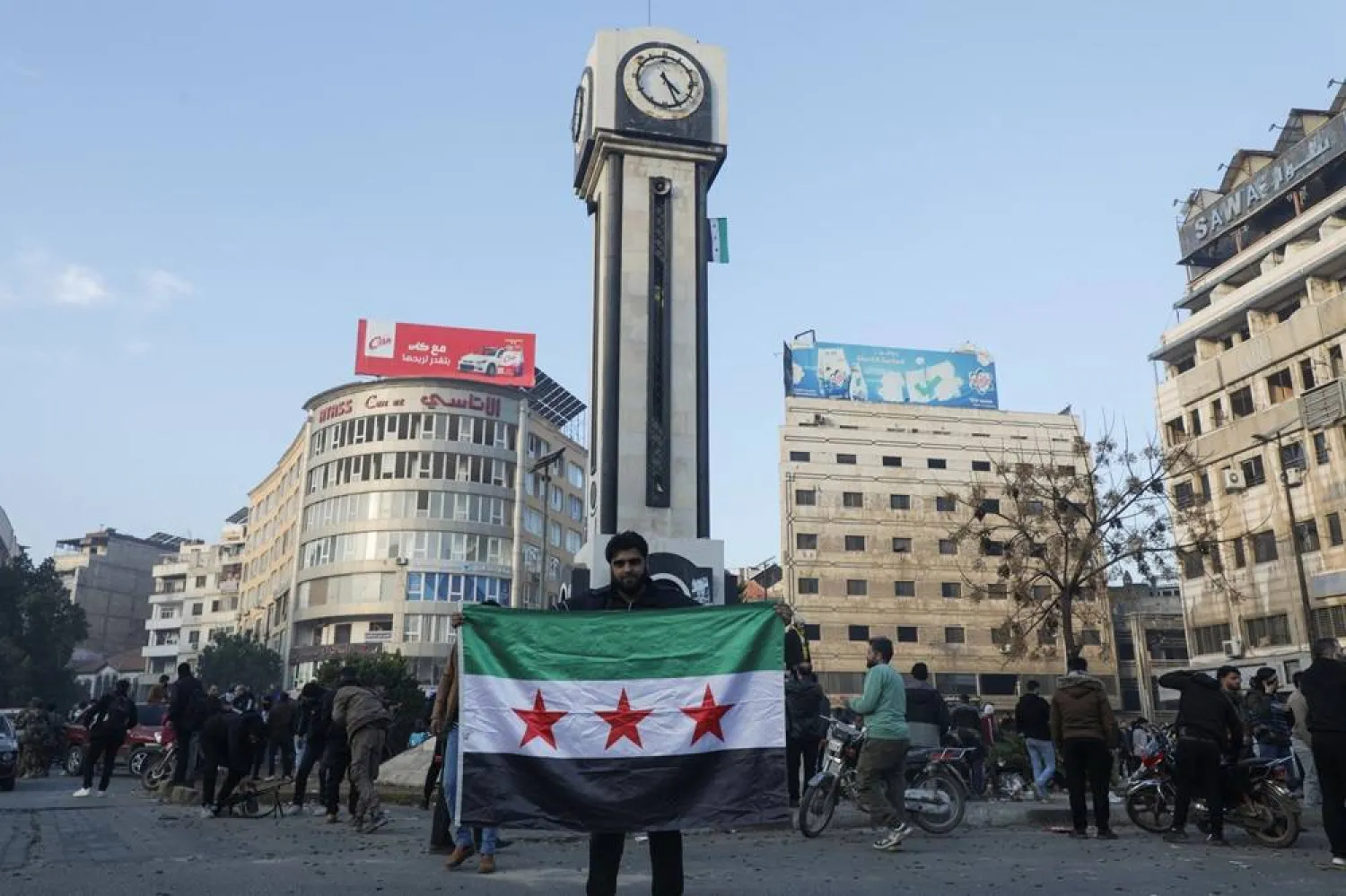 A man holds a Syrian opposition flag near the clock tower in Homs after Syria's army command notified officers on Sunday that President Bashar al-Assad's 24-year authoritarian rule has ended, in Homs, Syria December 8, 2024. (Reuters) 