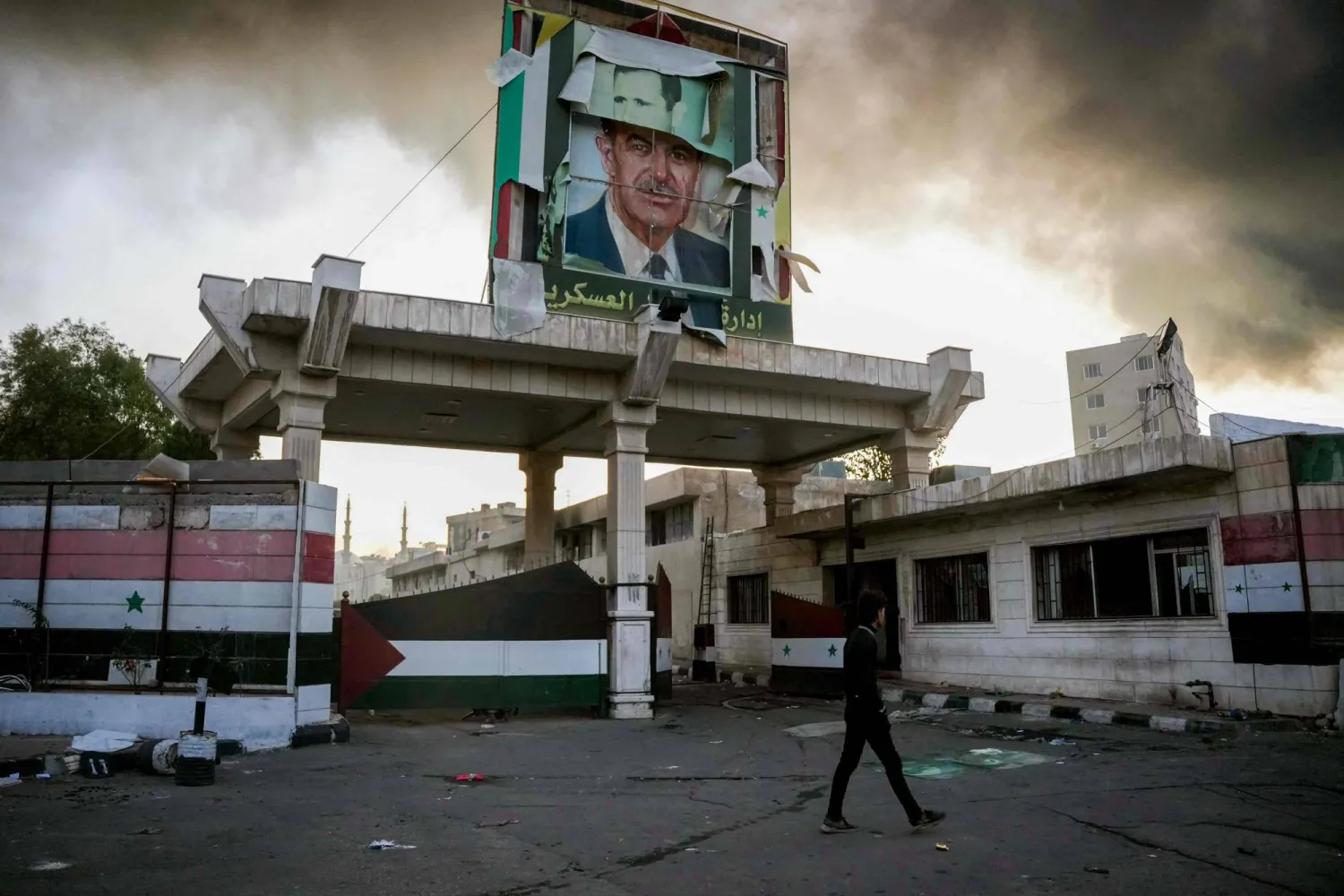 A defaced portrait of late Syrian president Hafez al-Assad stands above a ransacked government security facility, in Damascus, on December 8, 2024. (Photo by Rami al SAYED / AFP)