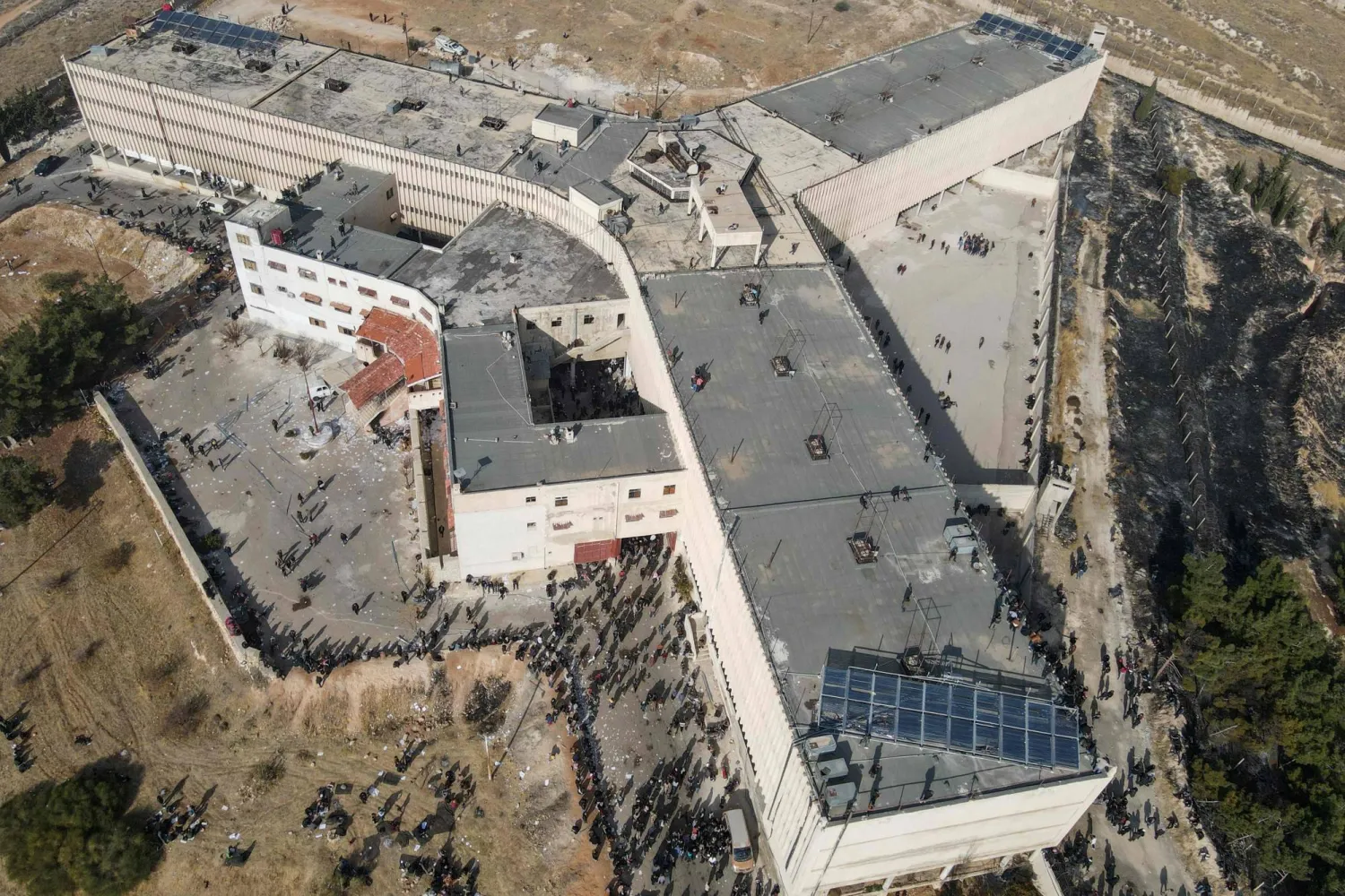 صورة جوية تظهر أشخاصاً يتجمعون بينما يبحث رجال الإنقاذ والخبراء عن أقبية مخفية محتملة في سجن صيدنايا في دمشق في 9 ديسمبر 2024 (أ.ف.ب)