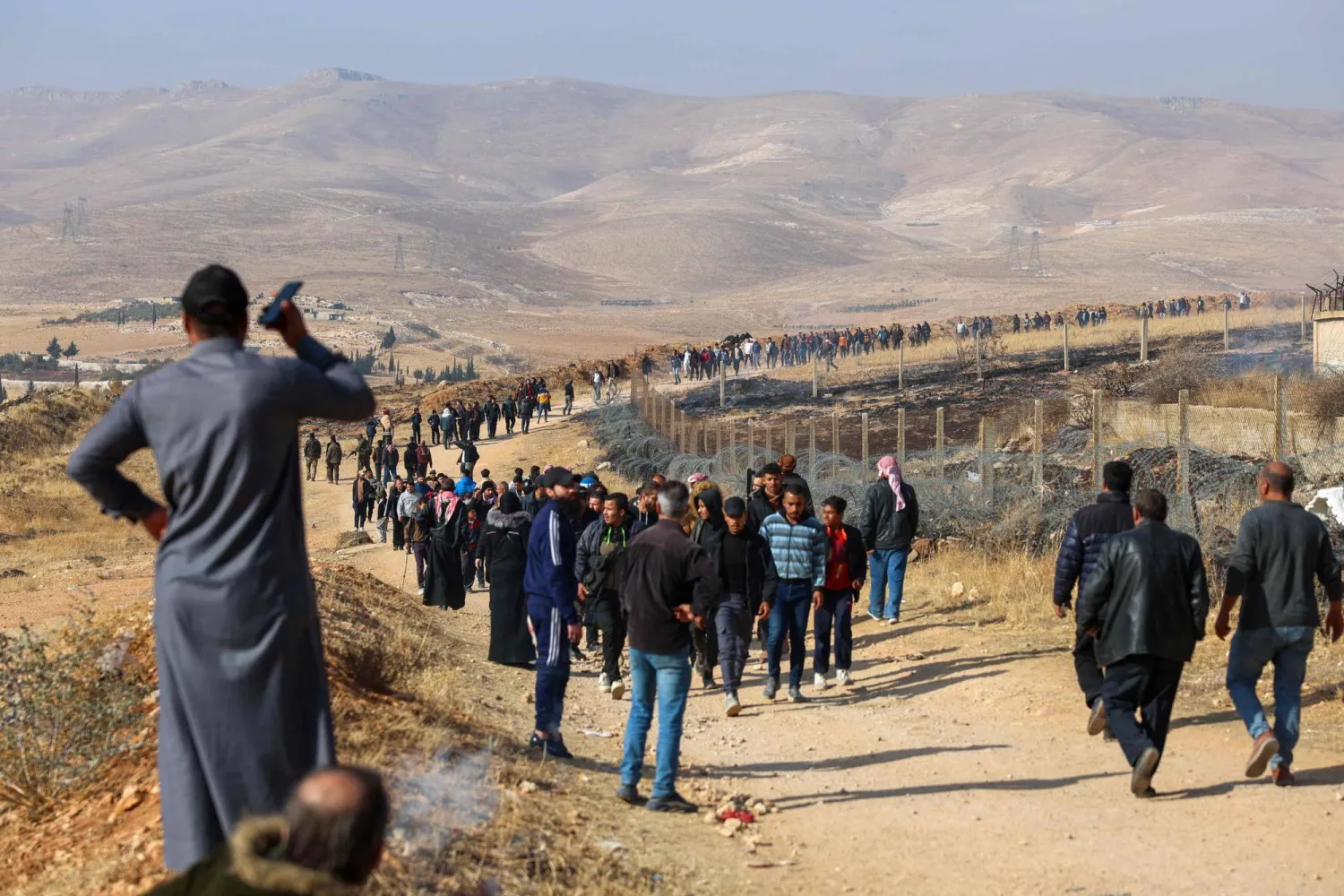 أشخاص يسيرون على طريق ترابي يؤدي إلى سجن صيدنايا في دمشق للبحث عن أحباء معتقلين 9 ديسمبر 2024 (أ.ف.ب)