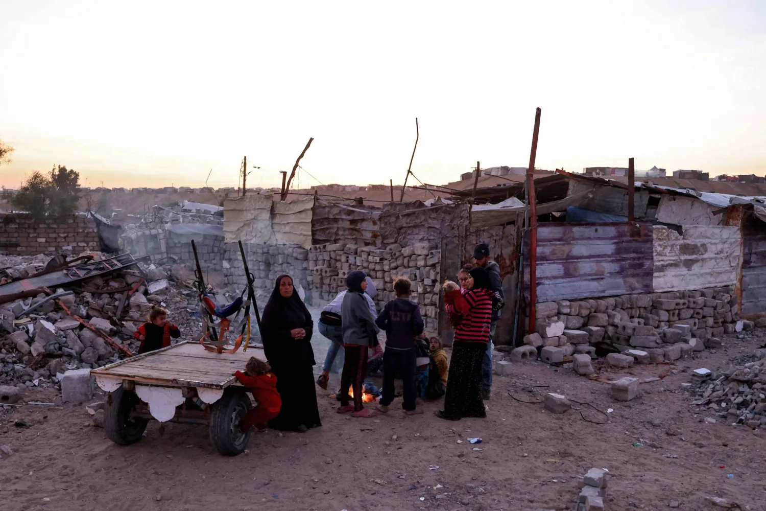 People keep warm by a fire at a makeshift camp for displaced Palestinians in the Nahr al-Bared area in Khan Yunis, in the southern Gaza Strip on December 9, 2024, amid the continuing war between Israel and the militant Hamas group. (Photo by Bashar TALEB / AFP)
