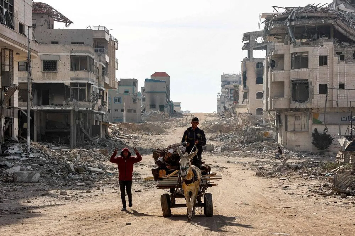 A youth gestures while walking next to a man driving a donkey-drawn cart loaded up with wood fragments to be used for firewood along a damaged street in Gaza City on December 11, 2024 amid the ongoing war in the Palestinian territory between Israel and Hamas. (AFP)