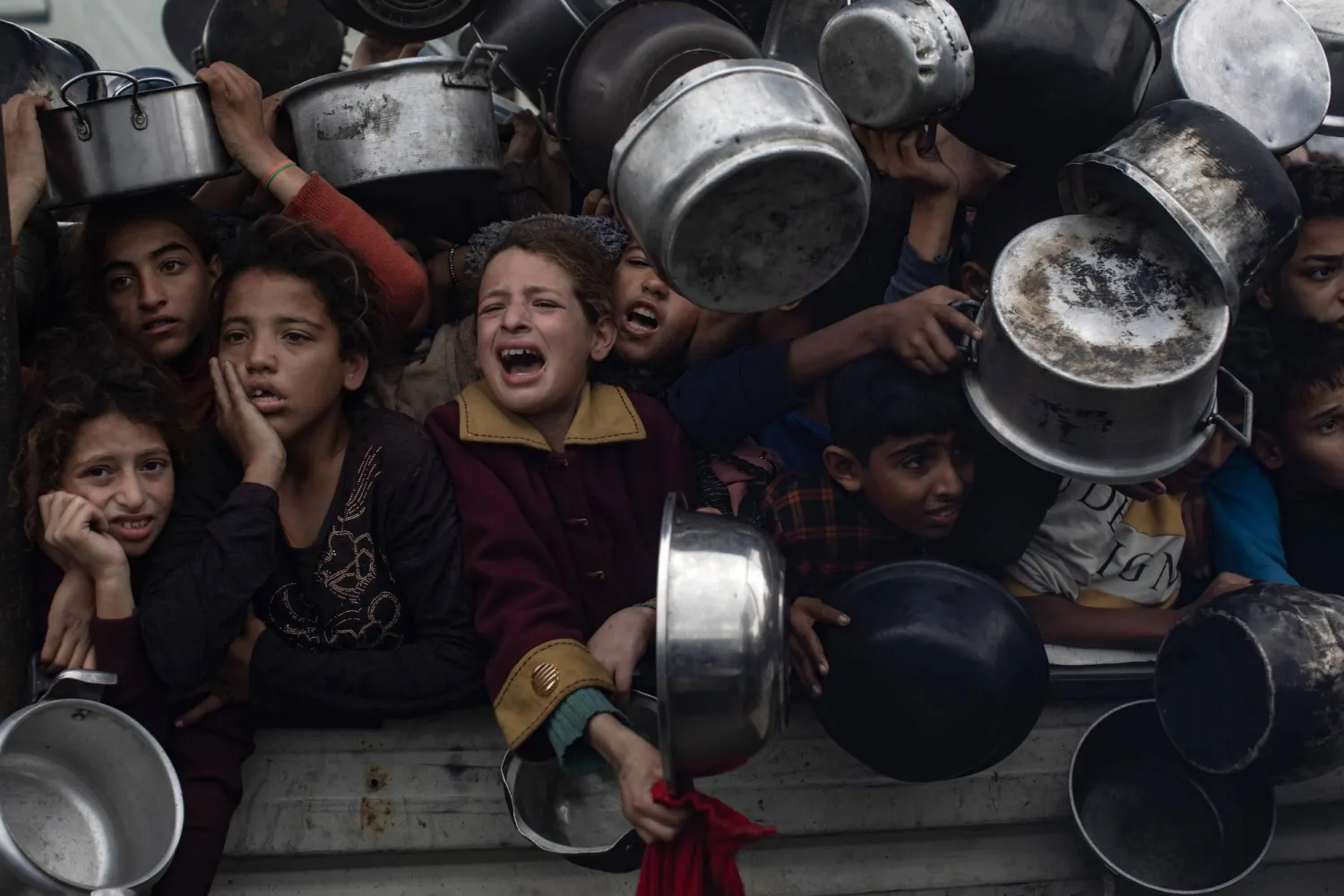 Palestinians, including children, hold metal pots and pans as they gather to receive food cooked by a charity kitchen, in Khan Yunis, southern Gaza Strip, 29 November 2024. EPA/HAITHAM IMAD