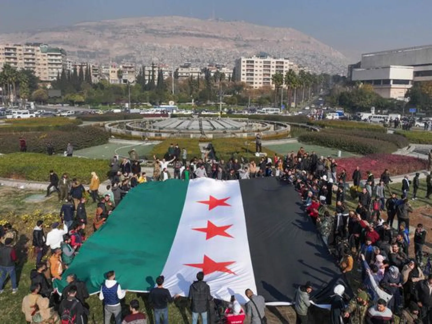 People celebrate with a large Syrian opposition flag at Umayyad Square in Damascus. OMAR HAJ KADOUR / AFP