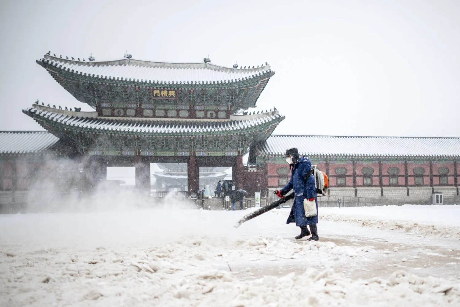 أحد الموظفين يعمل عند بوابة جوانج هوامون خلال تساقط الثلوج في سيول اليوم (أ.ف.ب)