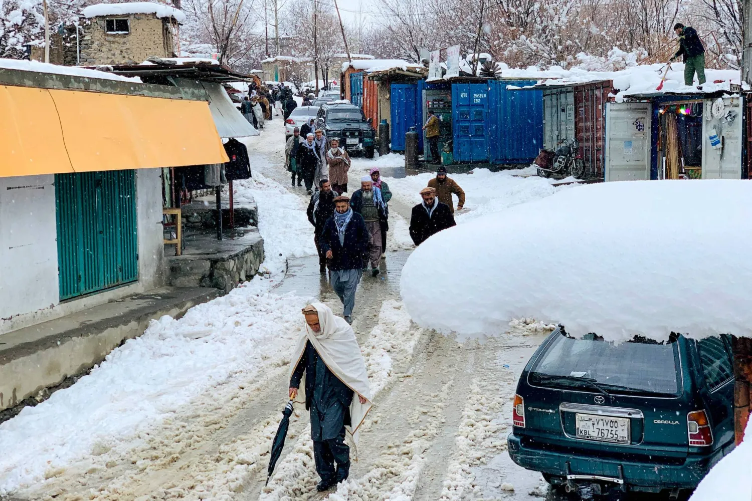 مواطنون أفغان يتجولون أمام متاجر في إحدى الأسواق خلال تساقط الثلوج بمنطقة دارا بولاية بنجشير (أ.ف.ب)