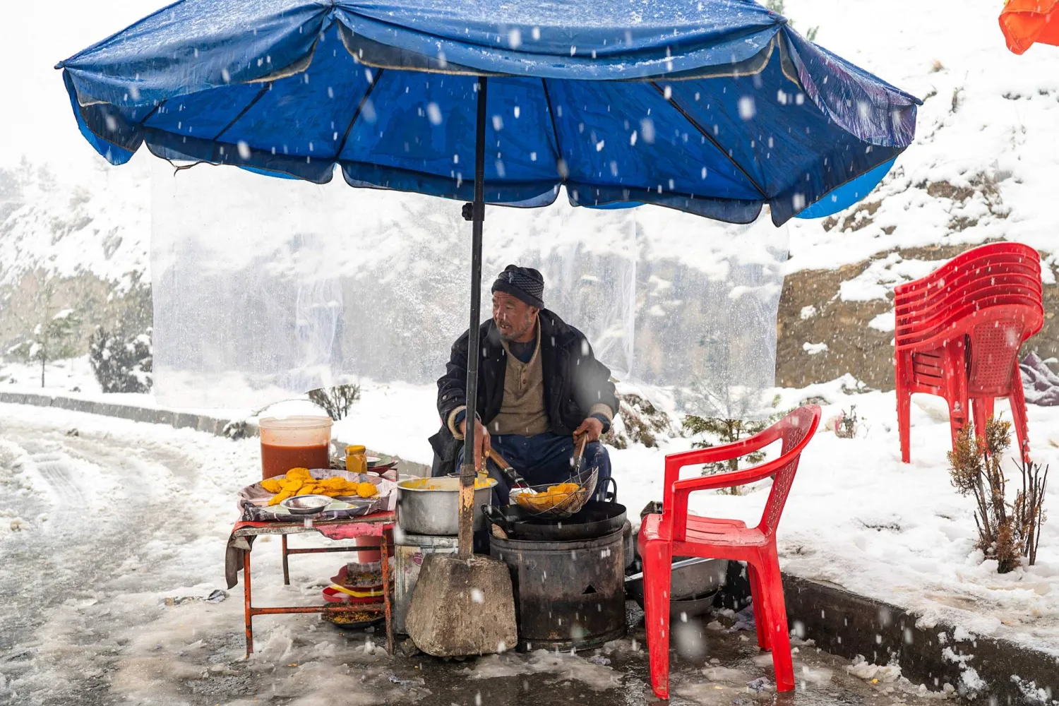 بائع أفغاني يعد الفطائر المحلية المعروفة باسم «باكورا» على طول أحد الشوارع خلال أول تساقط كثيف للثلوج هذا الشتاء في كابل (أ.ف.ب)