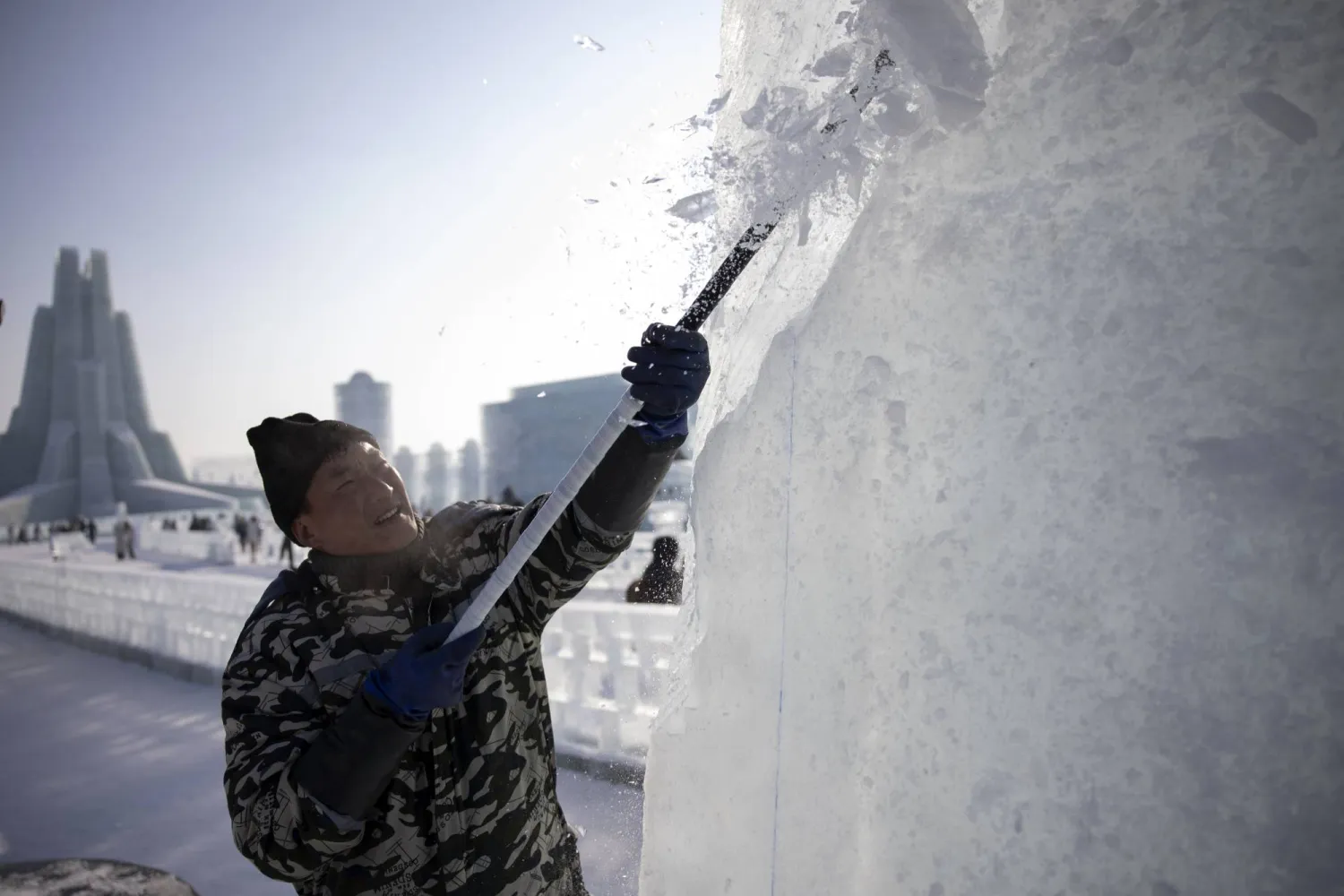 عامل ينحت كتلة من الجليد في مهرجان هاربين للجليد والثلج بمقاطعة هيلونغجيانغ بالصين (إ.ب.أ)