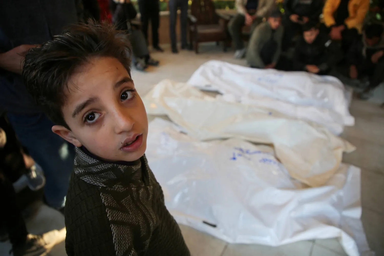 طفل يقف بجانب جثث فلسطينيين قُتلوا في غارات جوية إسرائيلية في مستشفى ناصر بخان يونس (رويترز)