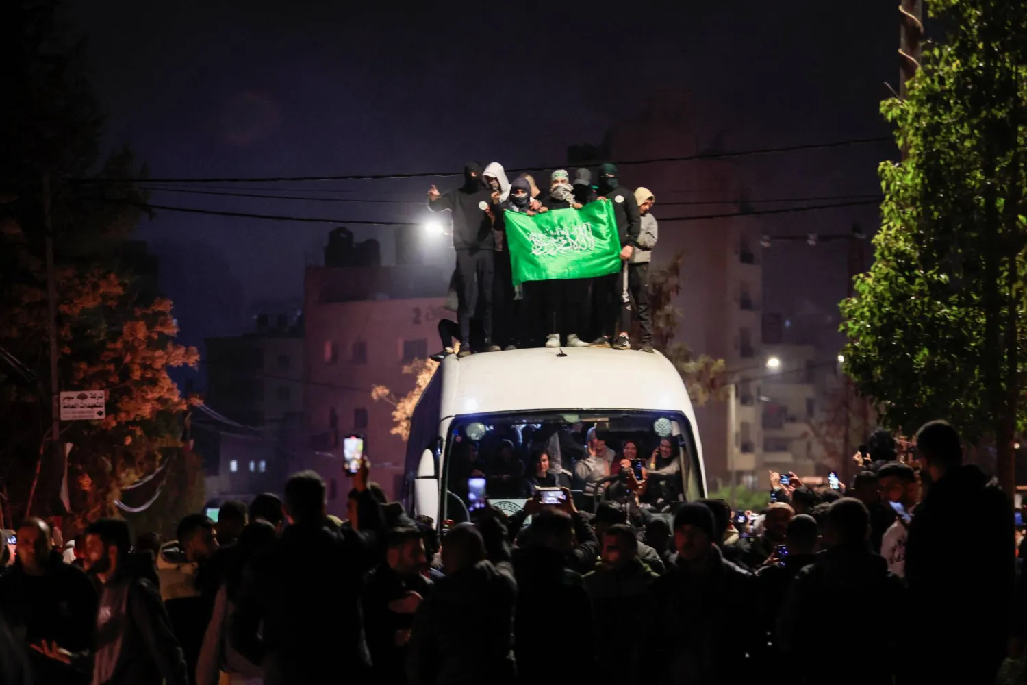 مواطنون يرفعون الأعلام أعلى حافلة تُقل عدداً من الأسرى في رام الله (رويترز)