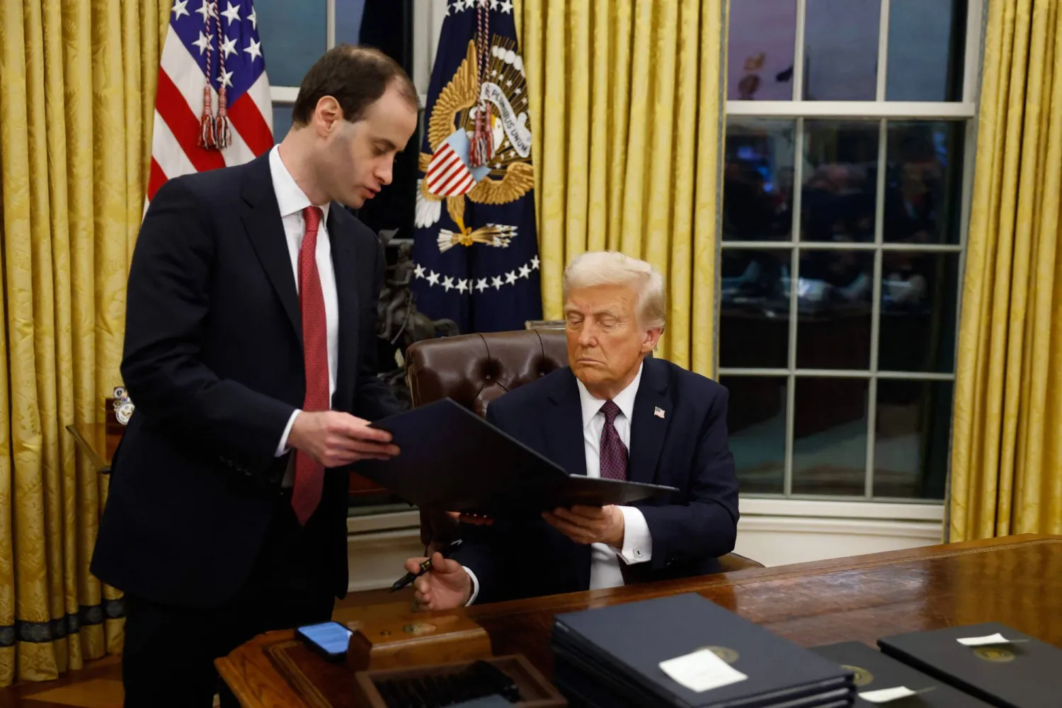 ترمب يوقّع أوامر تنفيذية في المكتب البيضاوي ويظهر الصندوق الخشبي إلى يمين الرئيس (أ.ف.ب)