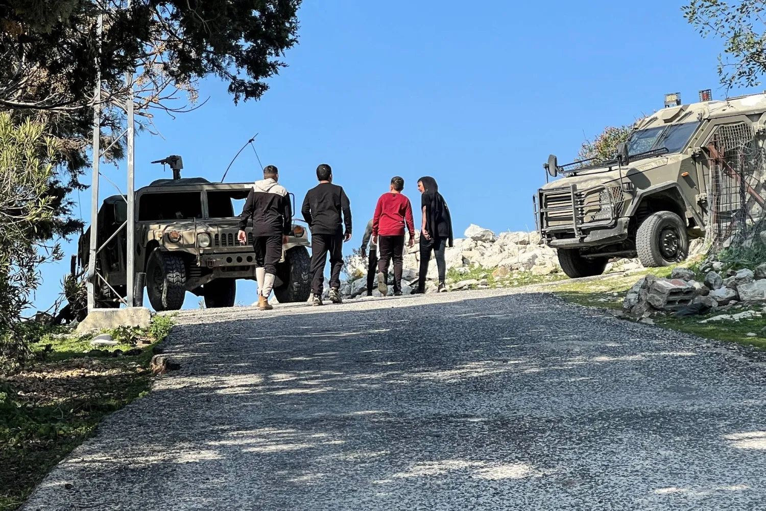 فتية في عرب العرامشة الحدودية مع لبنان يسيرون قرب آليات إسرائيلية بعد وقف إطلاق النار (رويترز)