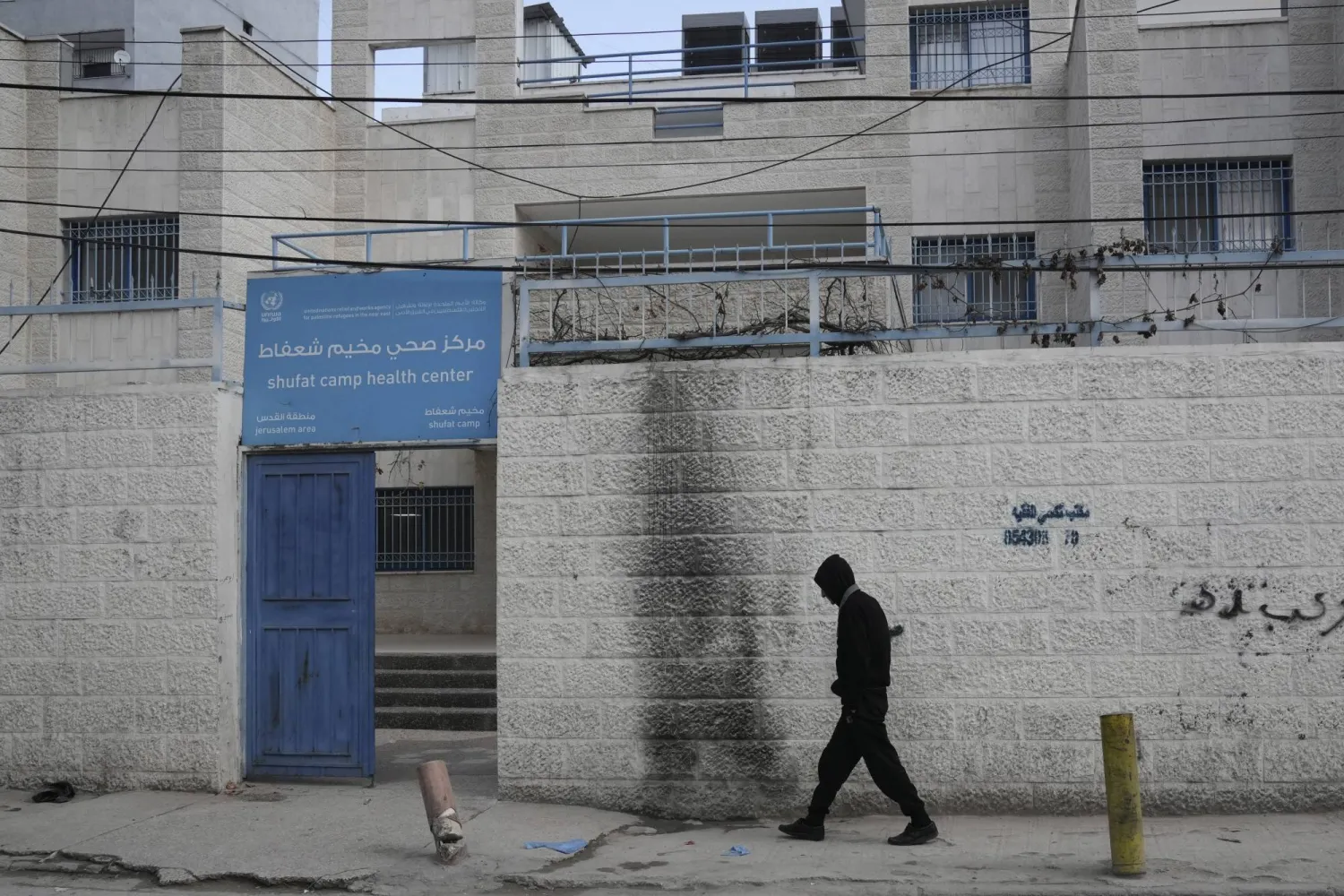 رجل يسير بالقرب من عيادة صحية تديرها وكالة الأمم المتحدة لإغاثة وتشغيل اللاجئين الفلسطينيين (أونروا) في مخيم شعفاط للاجئين في القدس - الاثنين 27 يناير 2025 (أسوشييتد برس)