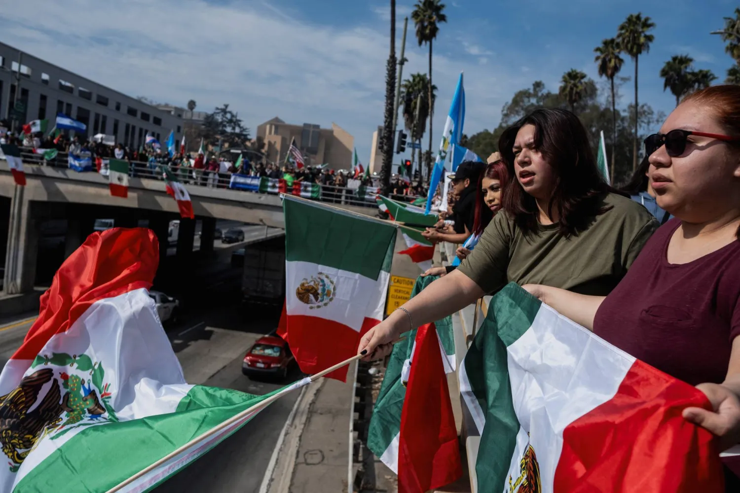 سيدات يلوحن بعلم المكسيك في أثناء مراقبتهن للطريق السريع 101 في الولايات المتحدة خلال احتجاج على اعتقال المهاجرين وترحيلهم من قبل وكالات الحكومة الأميركية في لوس أنجليس (رويترز)