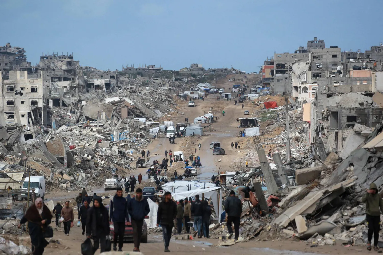 فلسطينيون نازحون يسيرون عبر طريق موحل وسط الدمار في جباليا شمال قطاع غزة الخميس خلال الهدنة بين إسرائيل و«حماس» (أ.ف.ب)