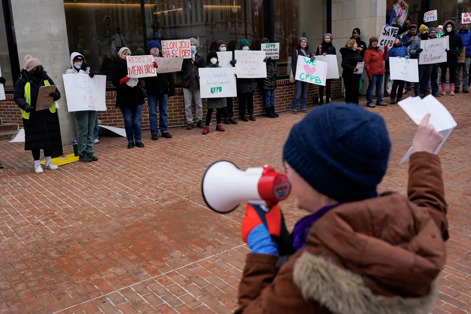 متظاهرون يحملون لافتات غداة انتقال أعضاء وزارة الكفاءة الحكومية إلى مكتب الحماية المالية للمستهلك في واشنطن السبت (رويترز)