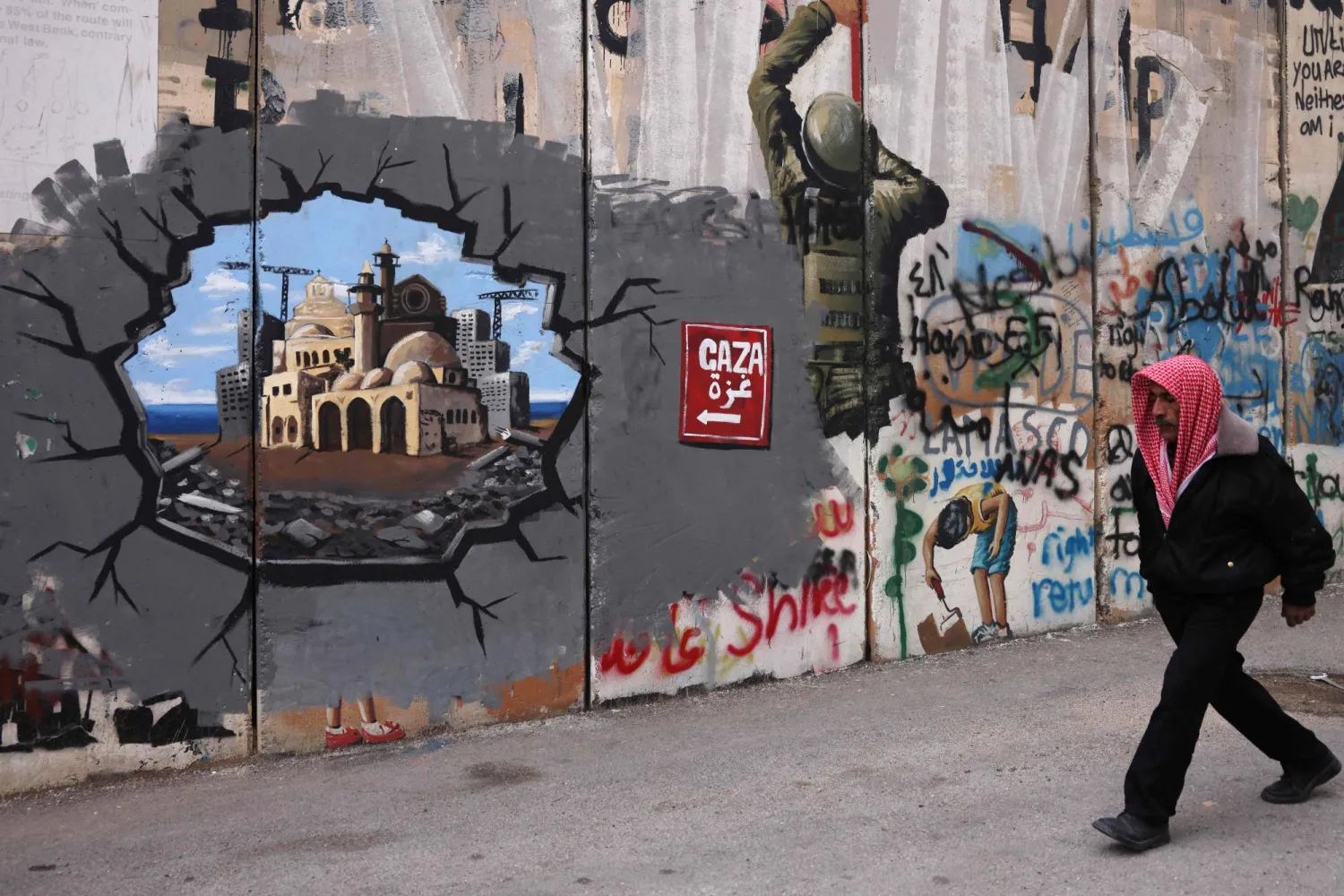 رجل يمشي أمام كتابات غرافيتي تمثل إعادة إعمار غزة (أ.ف.ب)