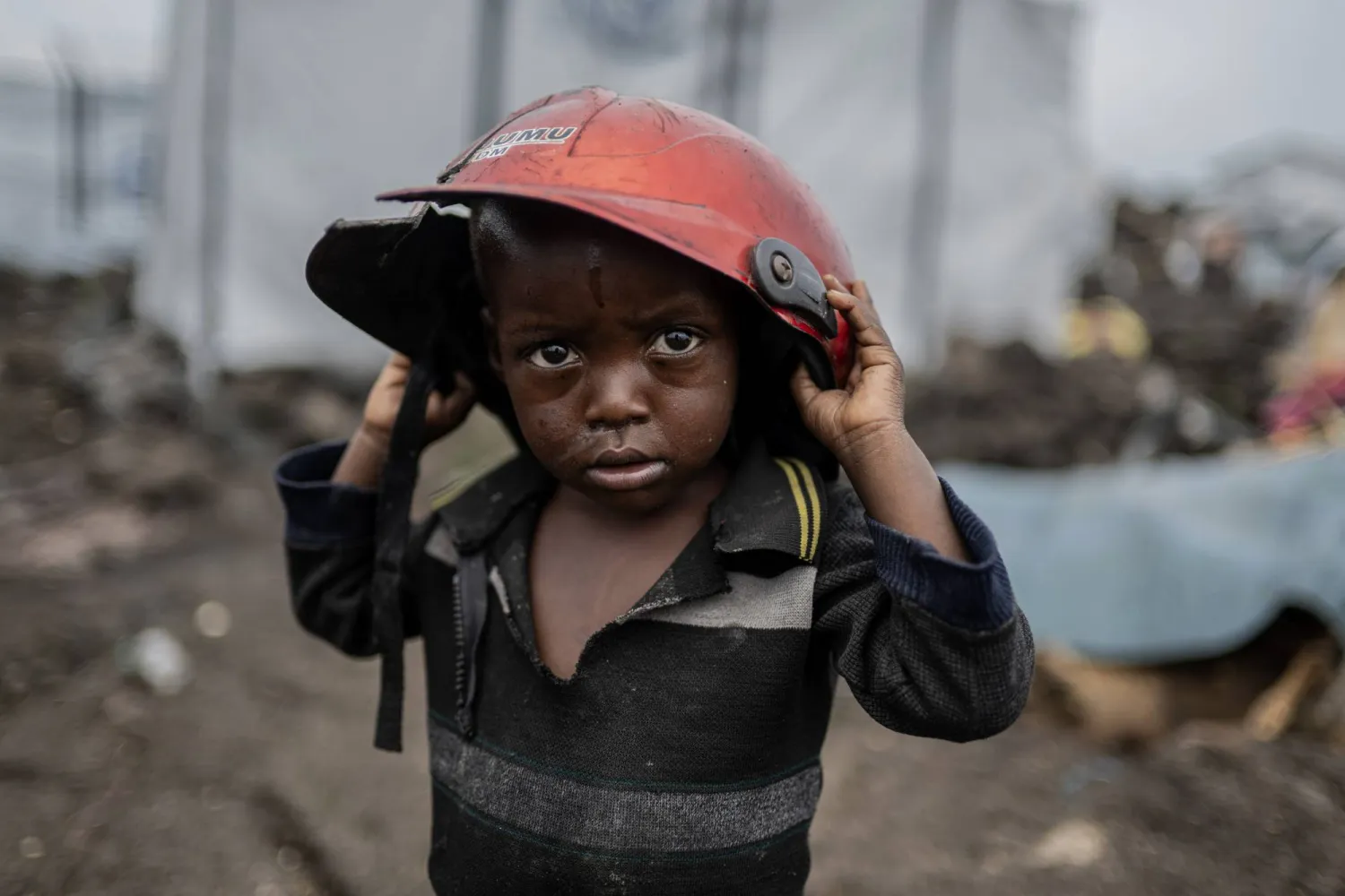 A child displaced by the fighting between M23 rebels and government soldiers holds a damaged helmet at the camp in Goma, Democratic Republic of the Congo, Tuesday, Feb. 11, 2025. (AP Photo/Moses Sawasawa)