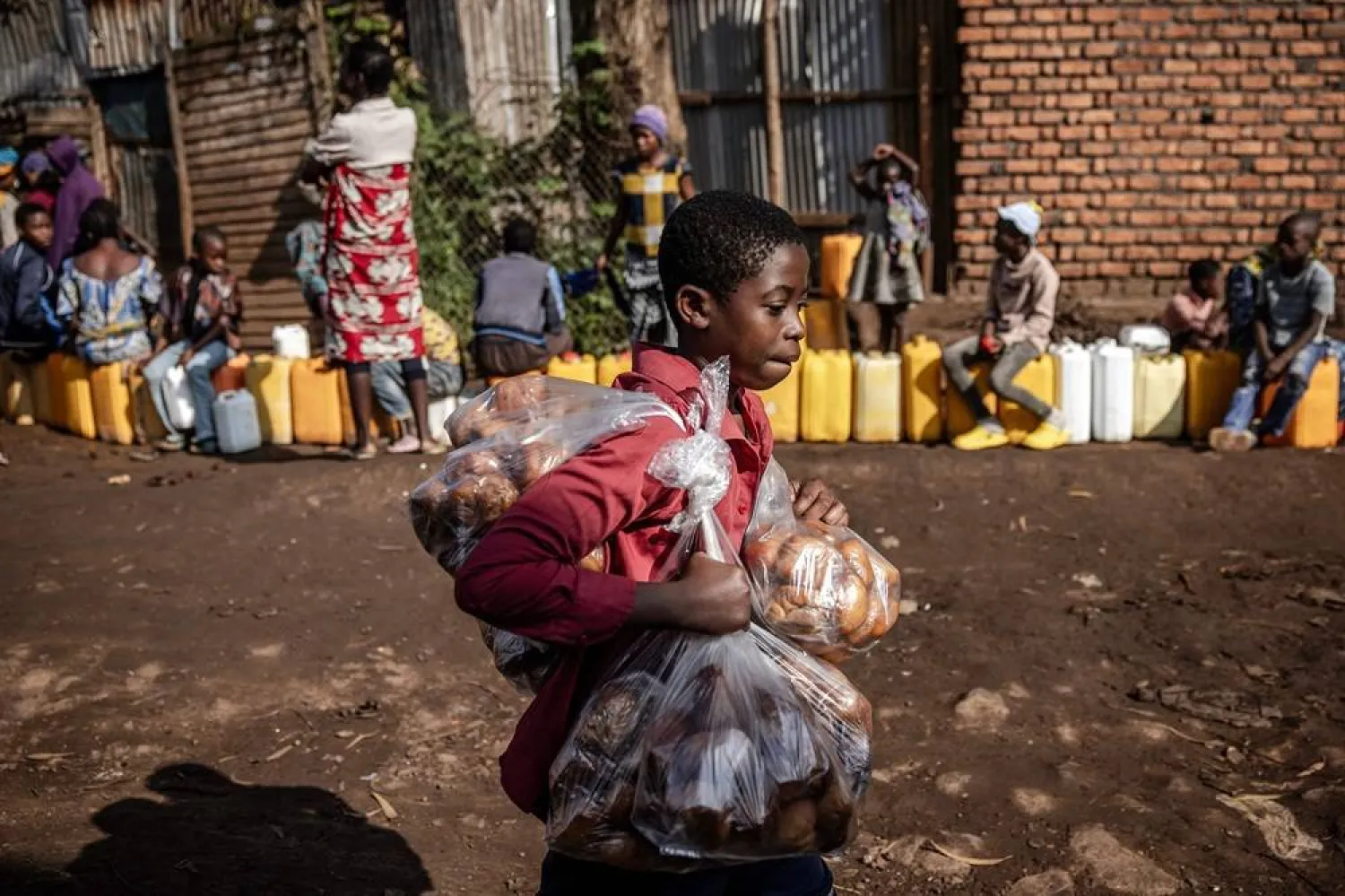 A boy sells snacks as residents queue with their water jars to collect water from a water point in Bukavu on February 21, 2025. (AFP)