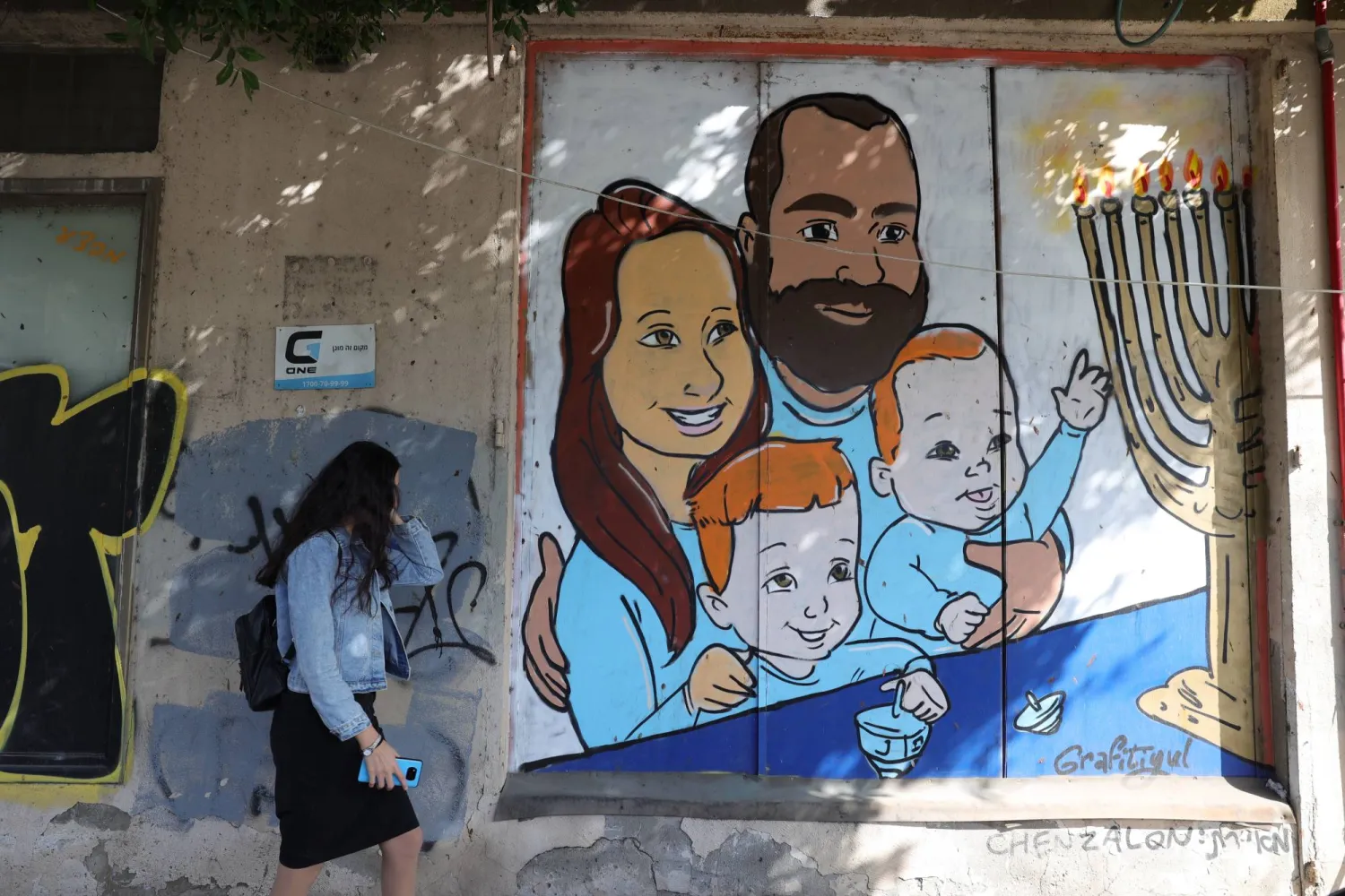 شابة تعبر برسم جداري لعائلة بيباس في وسط تل أبيب (إ.ب.أ)