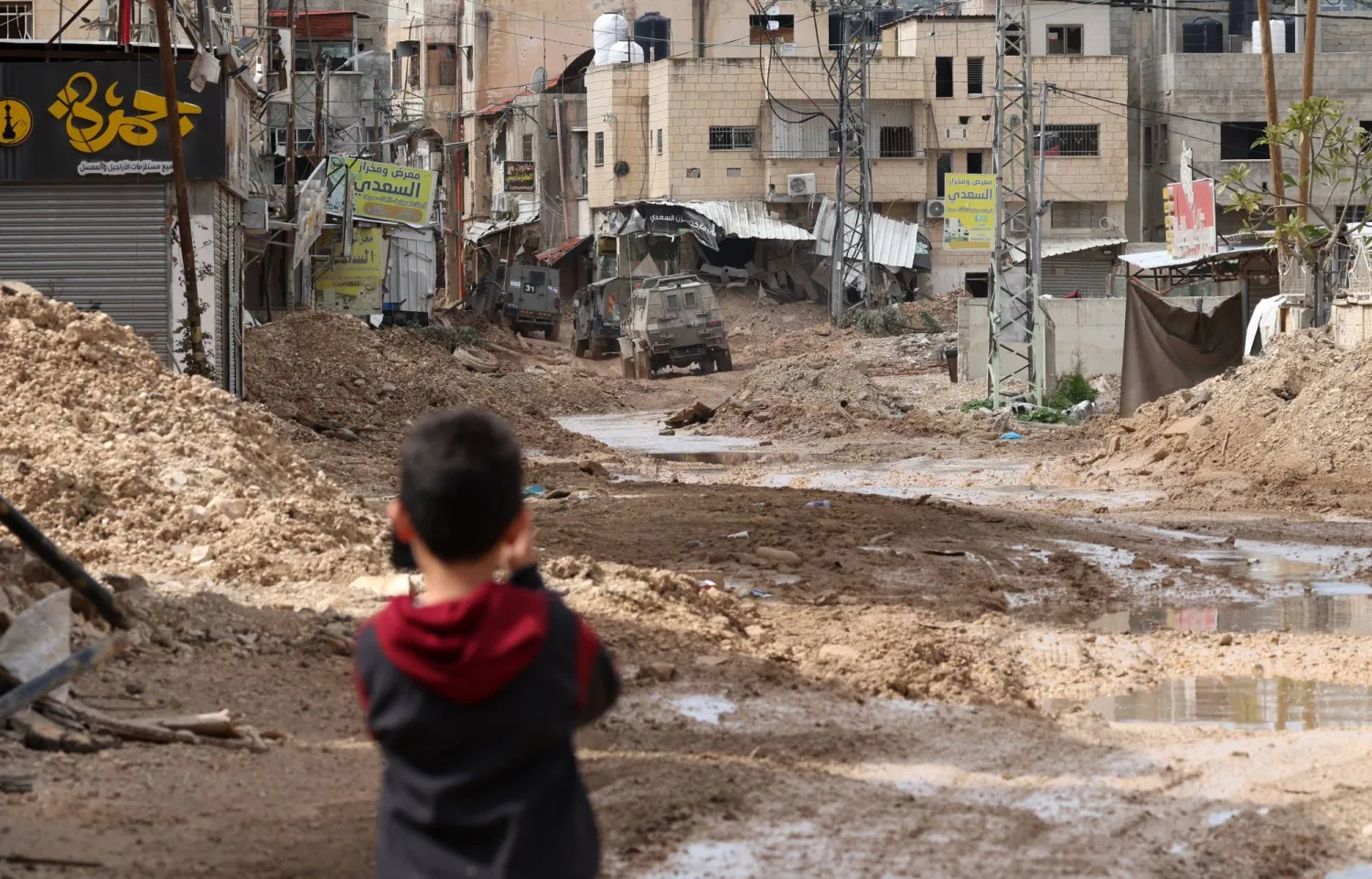طفل فلسطيني يشاهد توغل آليات الاحتلال الإسرائيلي في مخيم جنين الاثنين (إ.ب.أ)